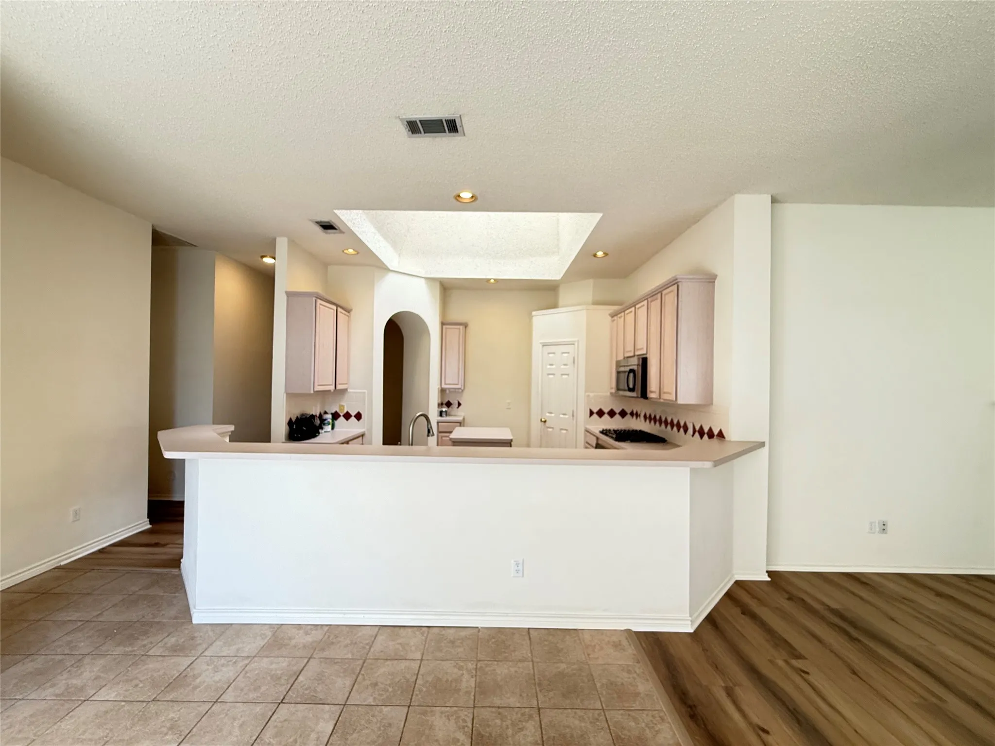Kitchen featuring a high breakfast bar, light wood-finish cabinetry, a built-in microwave, a skylight, and recessed lighting