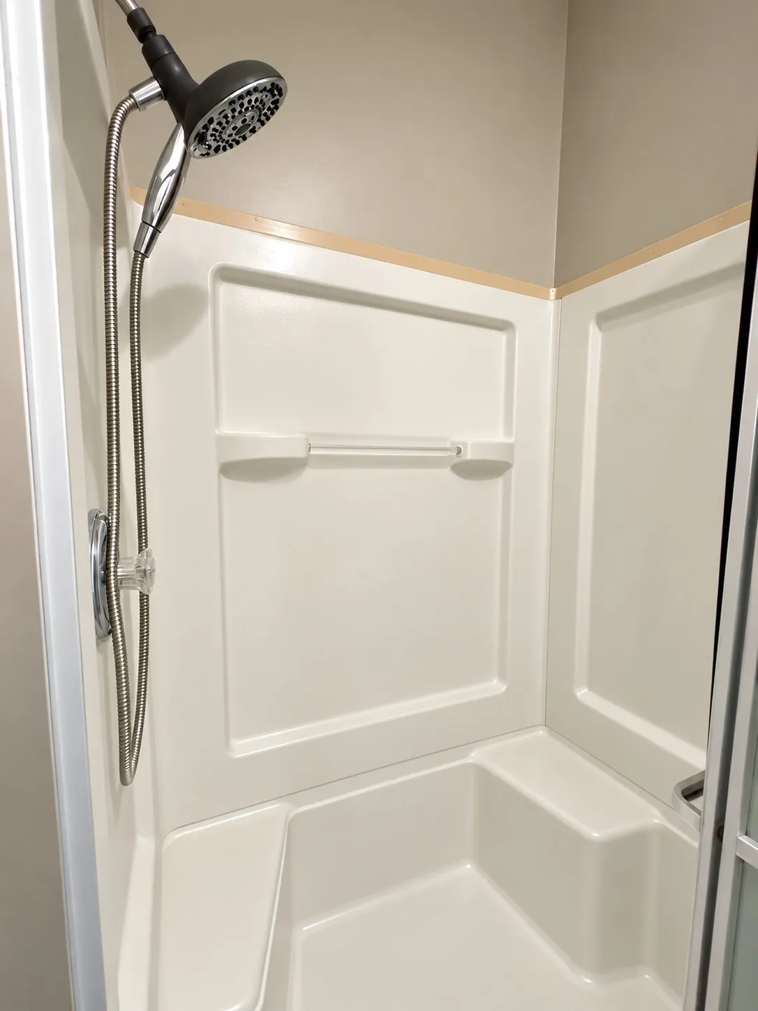 Primary. White fiberglass shower enclosure with an integrated seat, featuring a handheld showerhead and a chrome-finish faucet