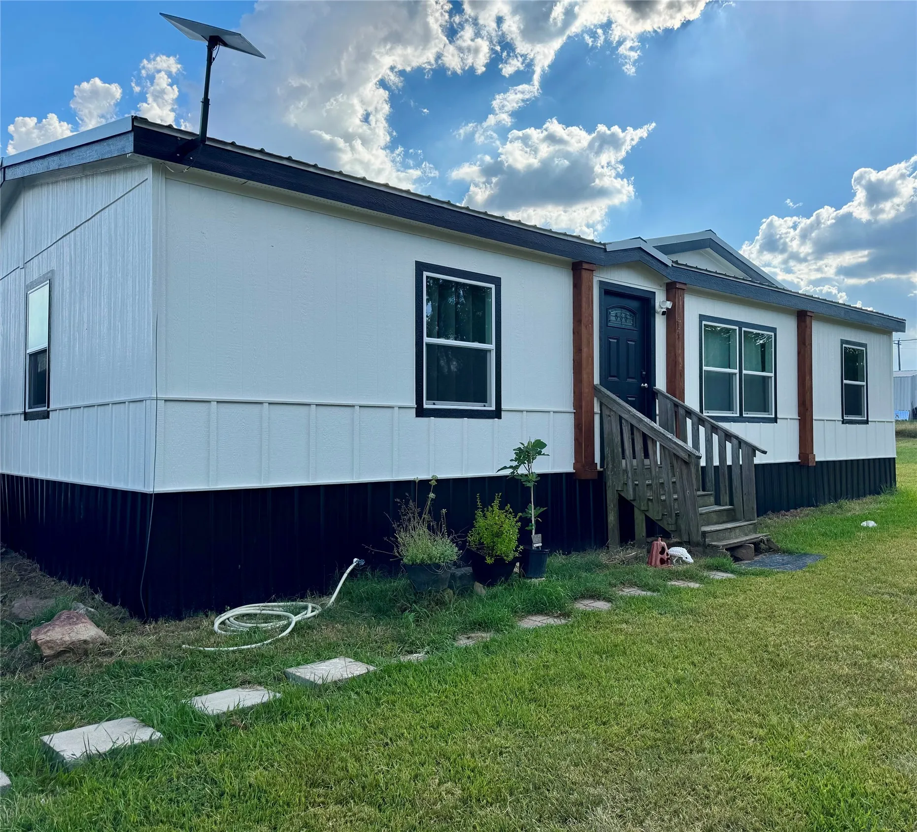 New Front Porch Coming Soon! White siding exterior with black trim windows, a dark entry door, and a wooden front porch with stairs
