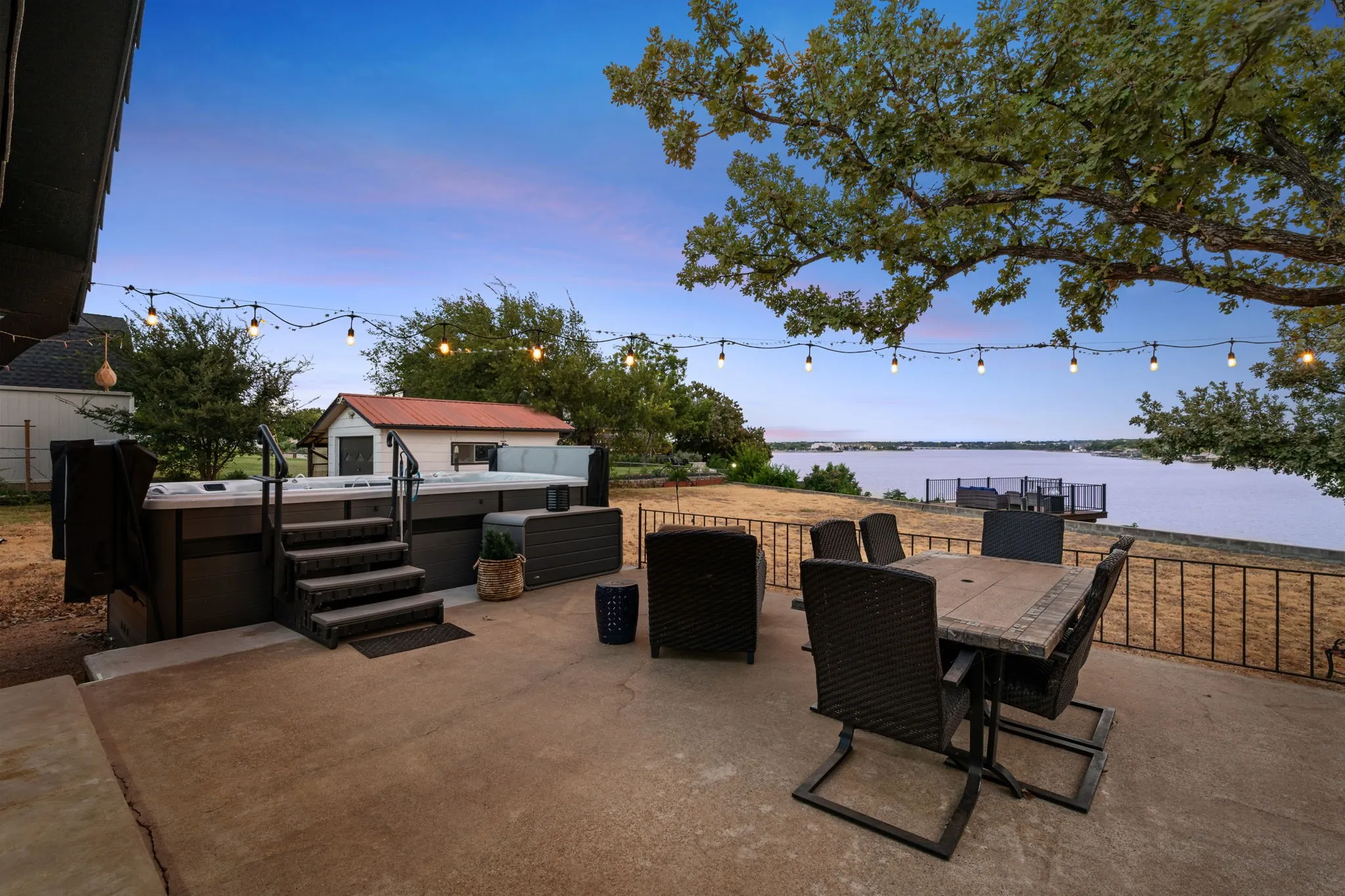 Expansive concrete patio featuring a built-in hot tub with steps and handrails, a dining area, and a wrought iron railing overlooking the water