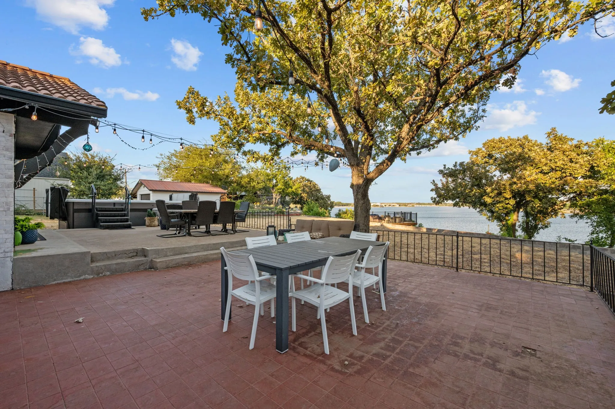 Expansive patio with terracotta-style pavers, a multi-level concrete deck, and a black metal railing overlooking the water