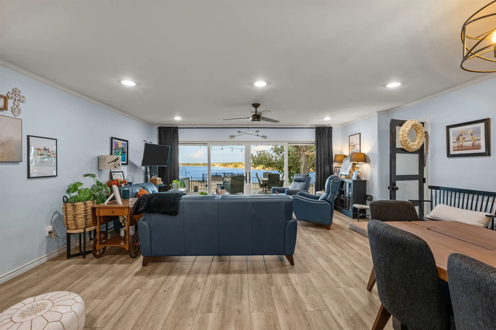 Recessed ceiling lights, wood-finish flooring, ceiling fan, and sliding glass doors opening to a scenic water backdrop