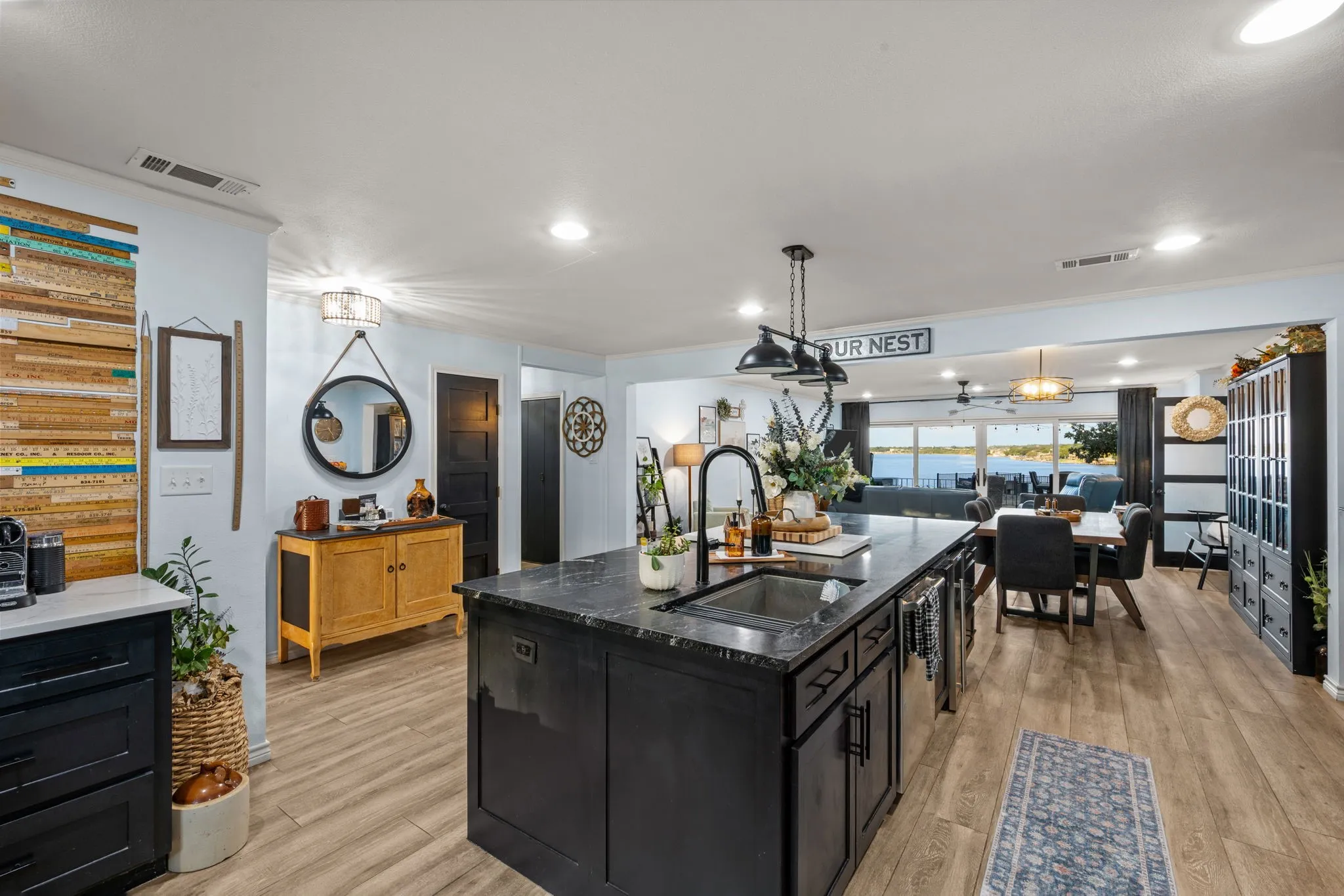 Open-concept kitchen and dining area featuring a large center island with sink, dark cabinetry, wood-finish flooring, and expansive windows