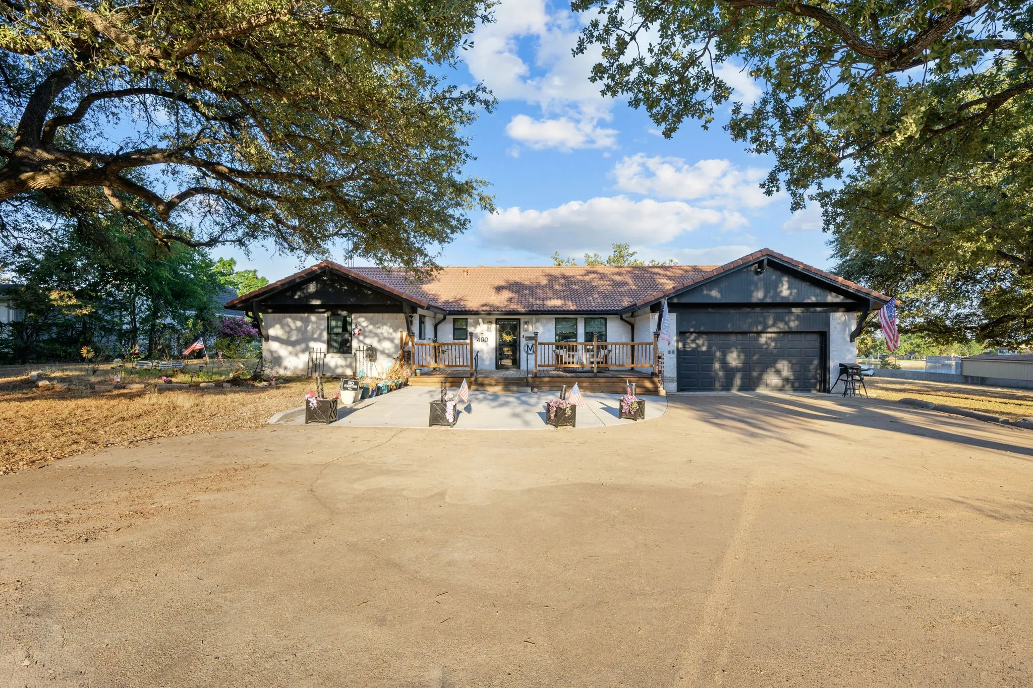 Exterior featuring a front porch with railing, attached two-car garage, and mature trees
