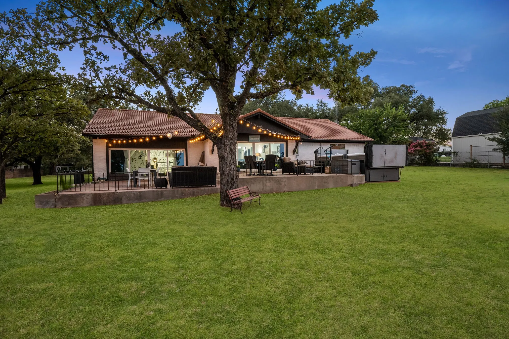 Expansive lawn with mature trees and a raised concrete patio featuring a black metal railing
