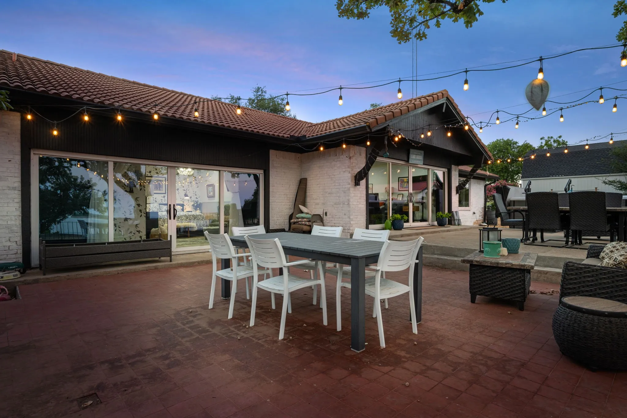 Expansive brick paver patio featuring a tile roof, white brick exterior, and multiple glass sliding doors