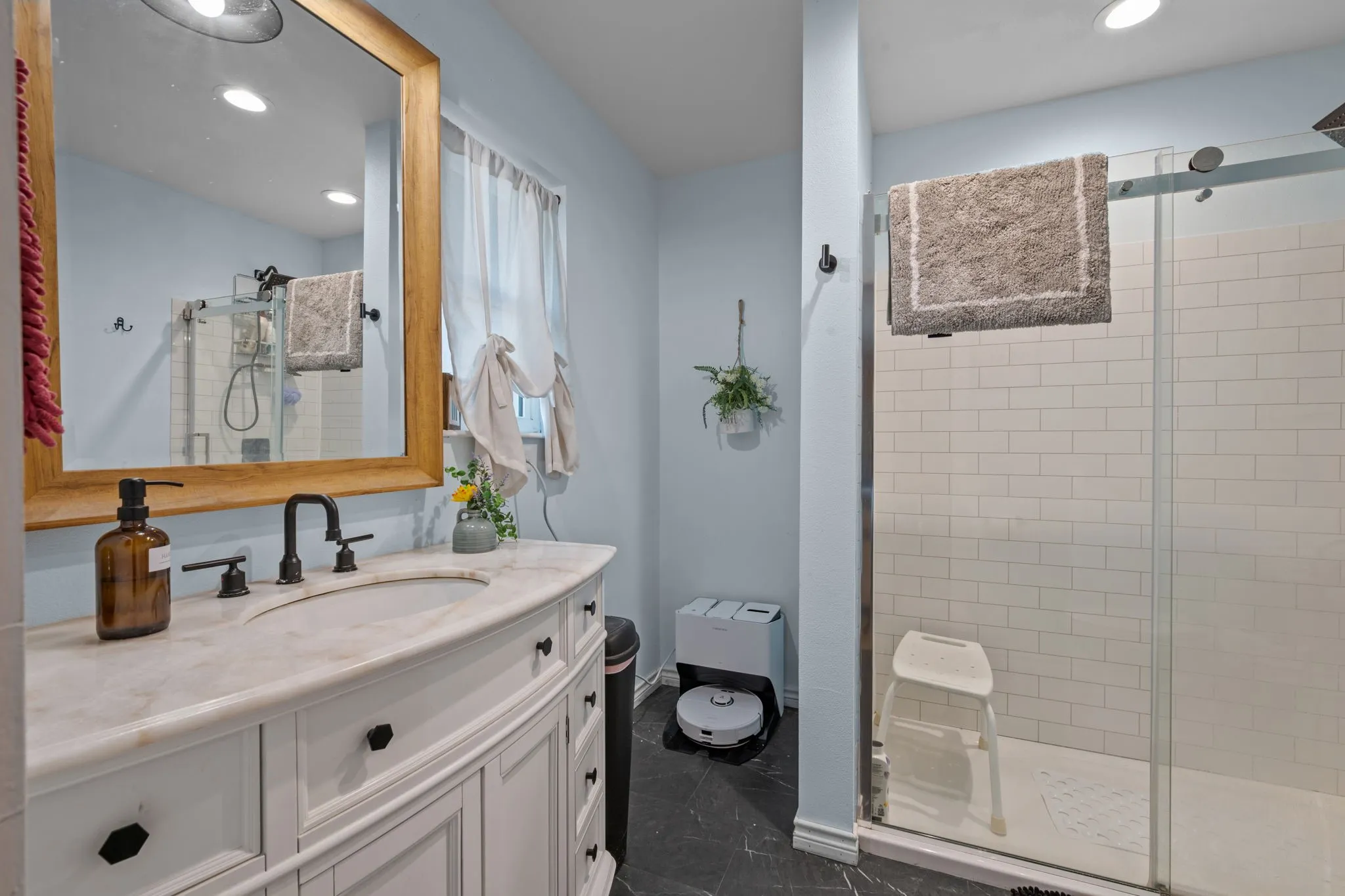 White vanity with a light-toned countertop, a black matte faucet, and a large wood-framed mirror