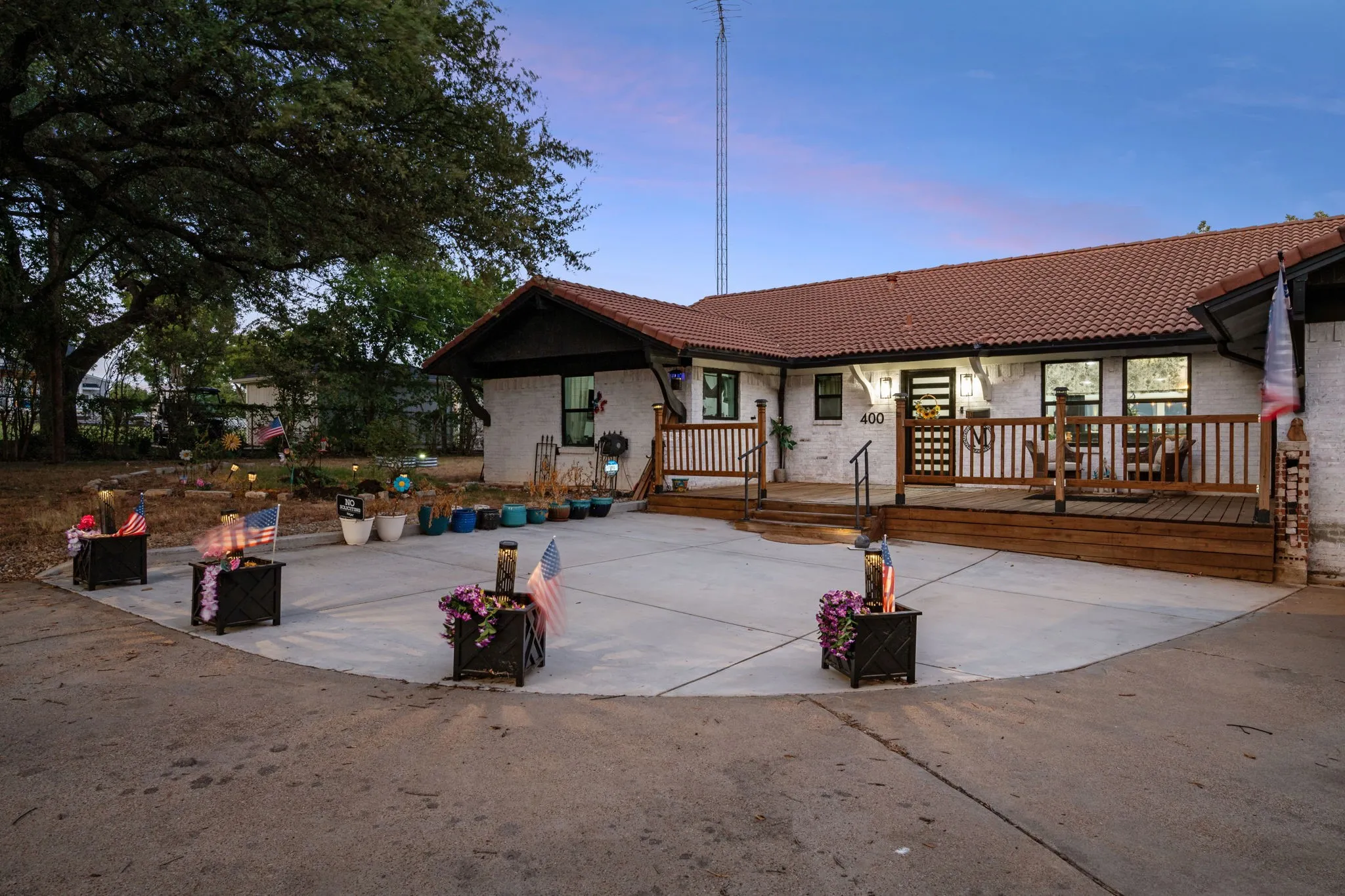 Exterior featuring a tile roof, painted brick facade, wood deck, and an expansive concrete driveway