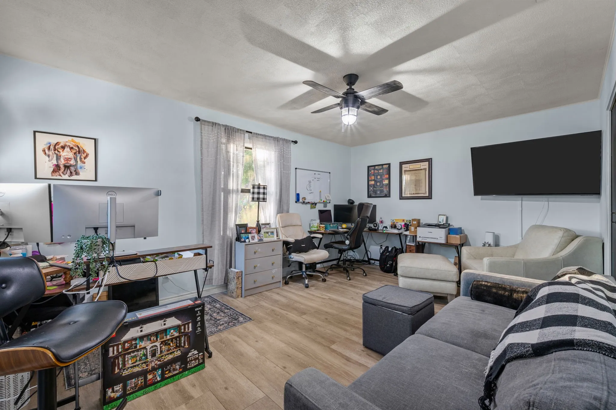 Wood-finish flooring throughout, ceiling fan with integrated lighting, and multiple windows with curtain rods