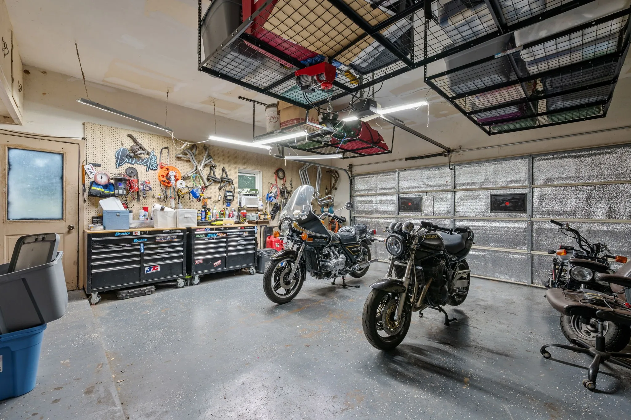 Garage featuring an epoxy coated floor, overhead storage racks, a workbench area with built-in cabinetry, and task lighting
