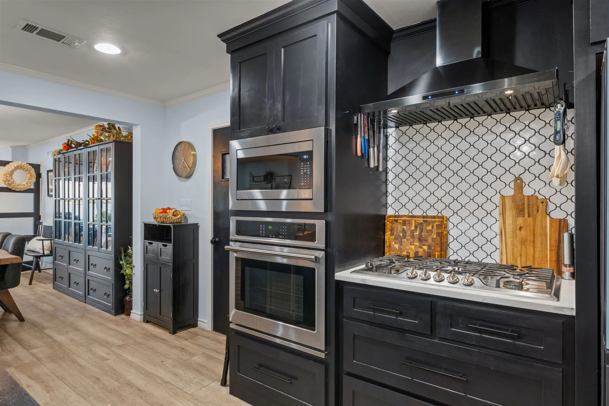Black cabinetry with stainless steel appliances, a built-in microwave and oven, a gas range with a stainless steel vent hood, and a white arabesque tile backsplash