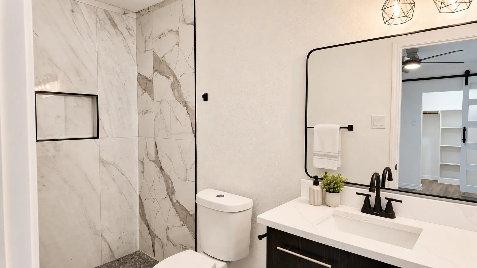 Walk-in shower with marble-look tile, recessed niche, and matte black fixtures. Decor is virtually staged.