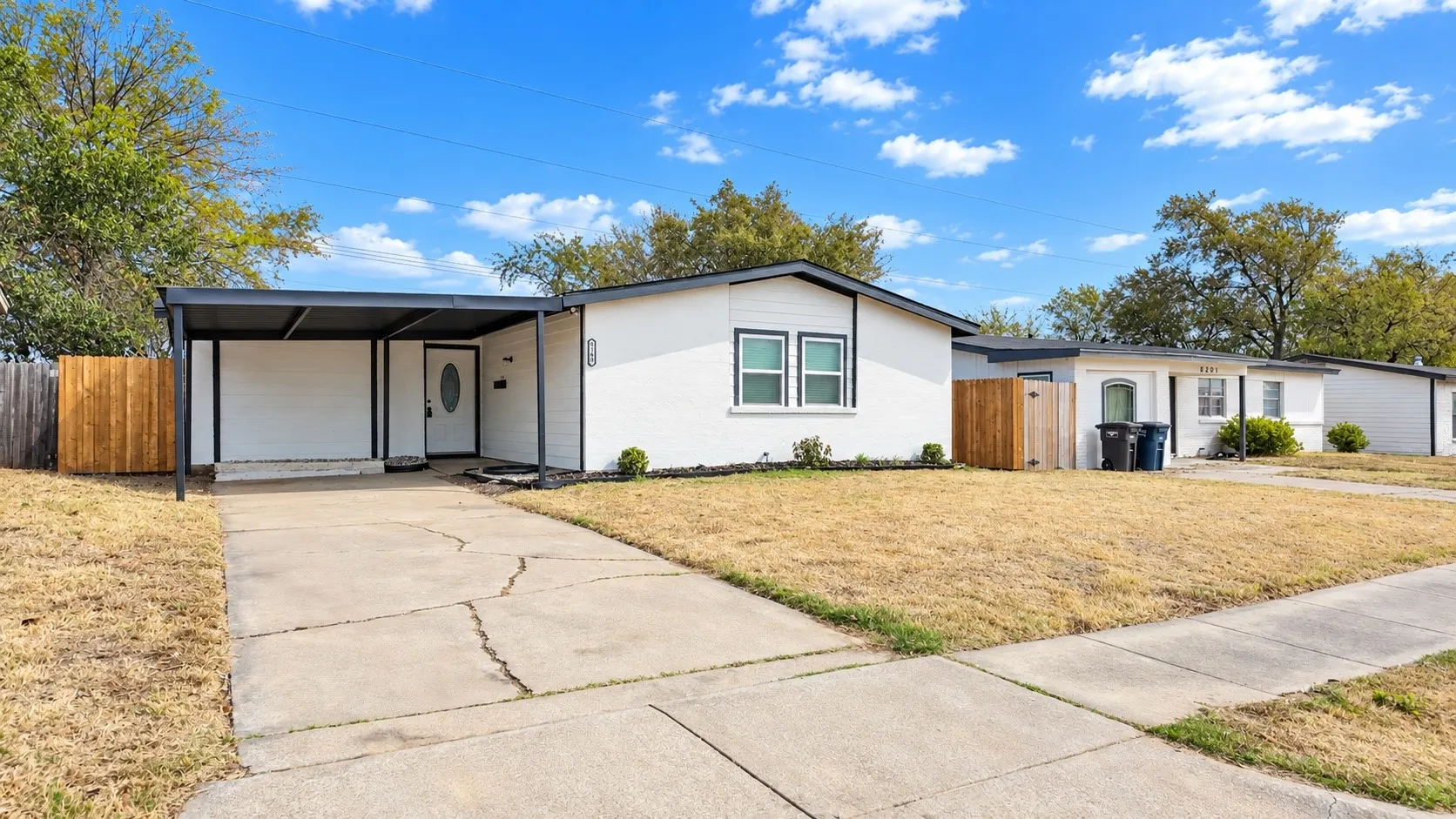 Angled front view showing the driveway, covered carport, and fenced side.
