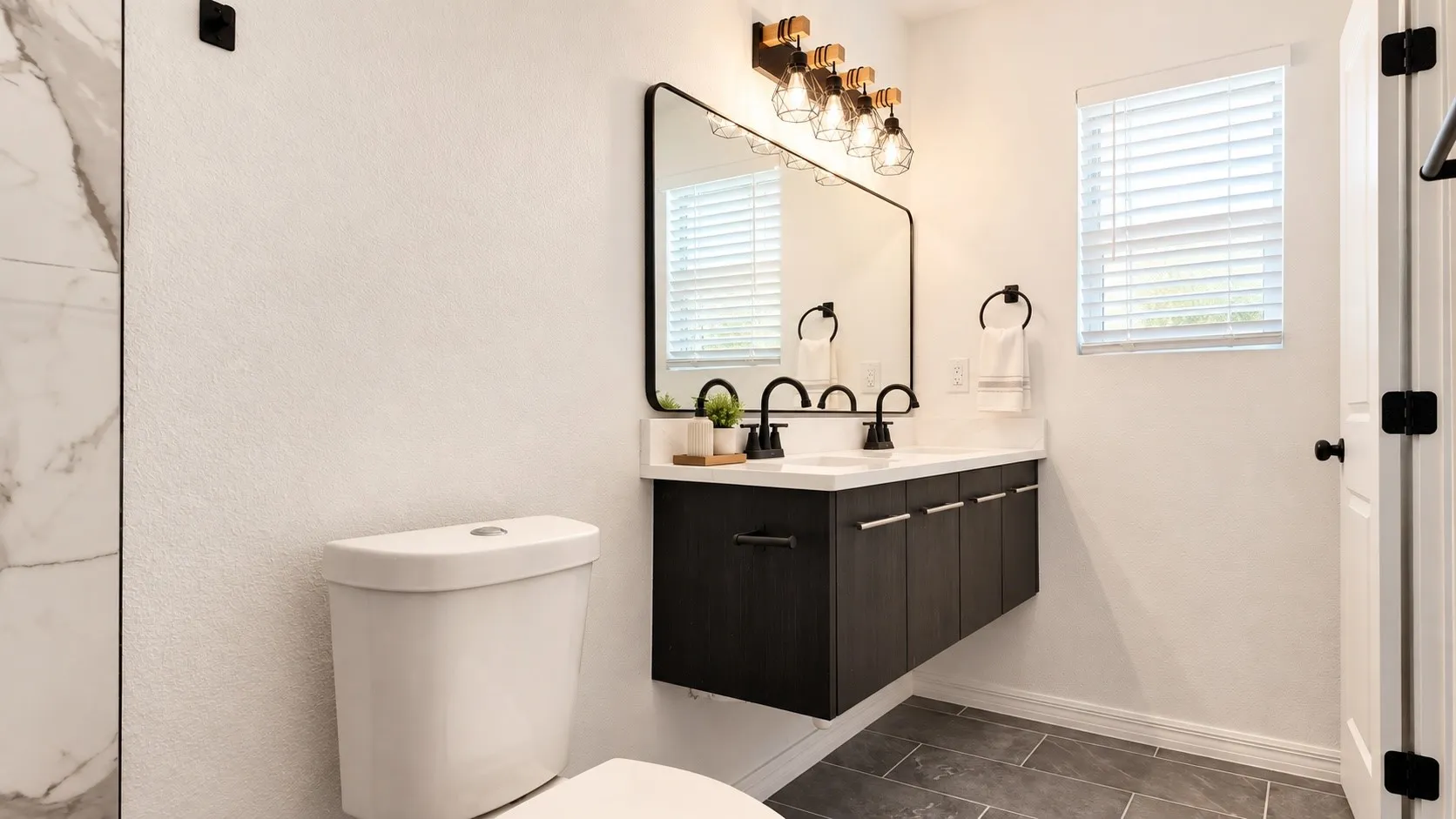 Ensuite bath with double floating vanity, black fixtures, and warm modern finishes. Decor is virtually staged.