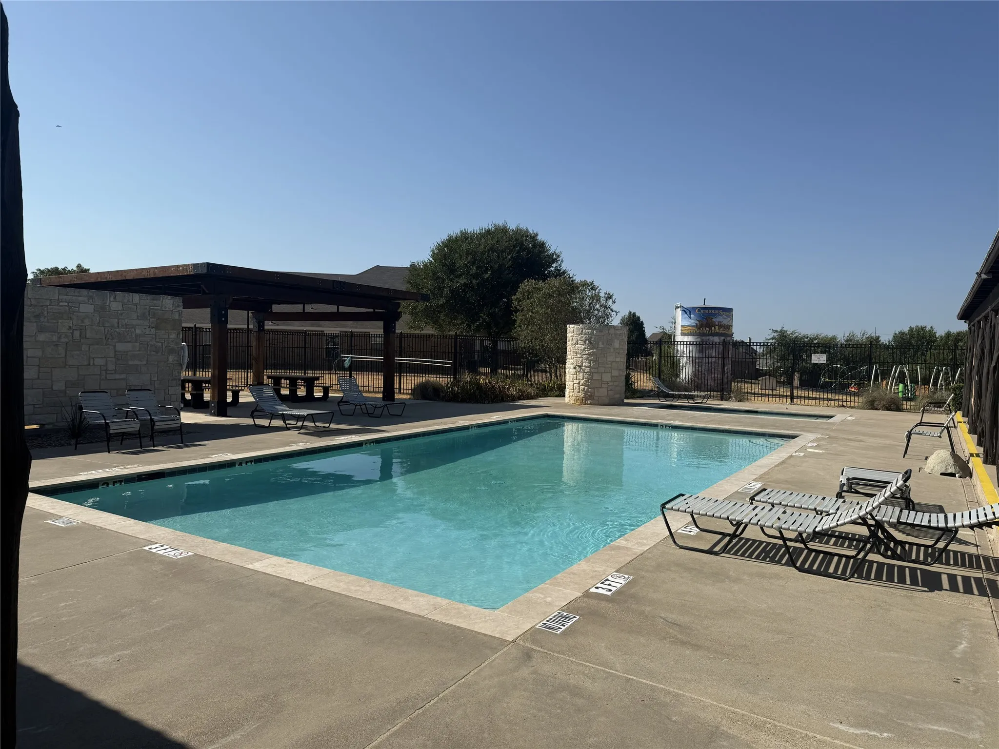 Community swimming pool featuring a large concrete deck, a stone-clad privacy wall, and a shaded pergola structure