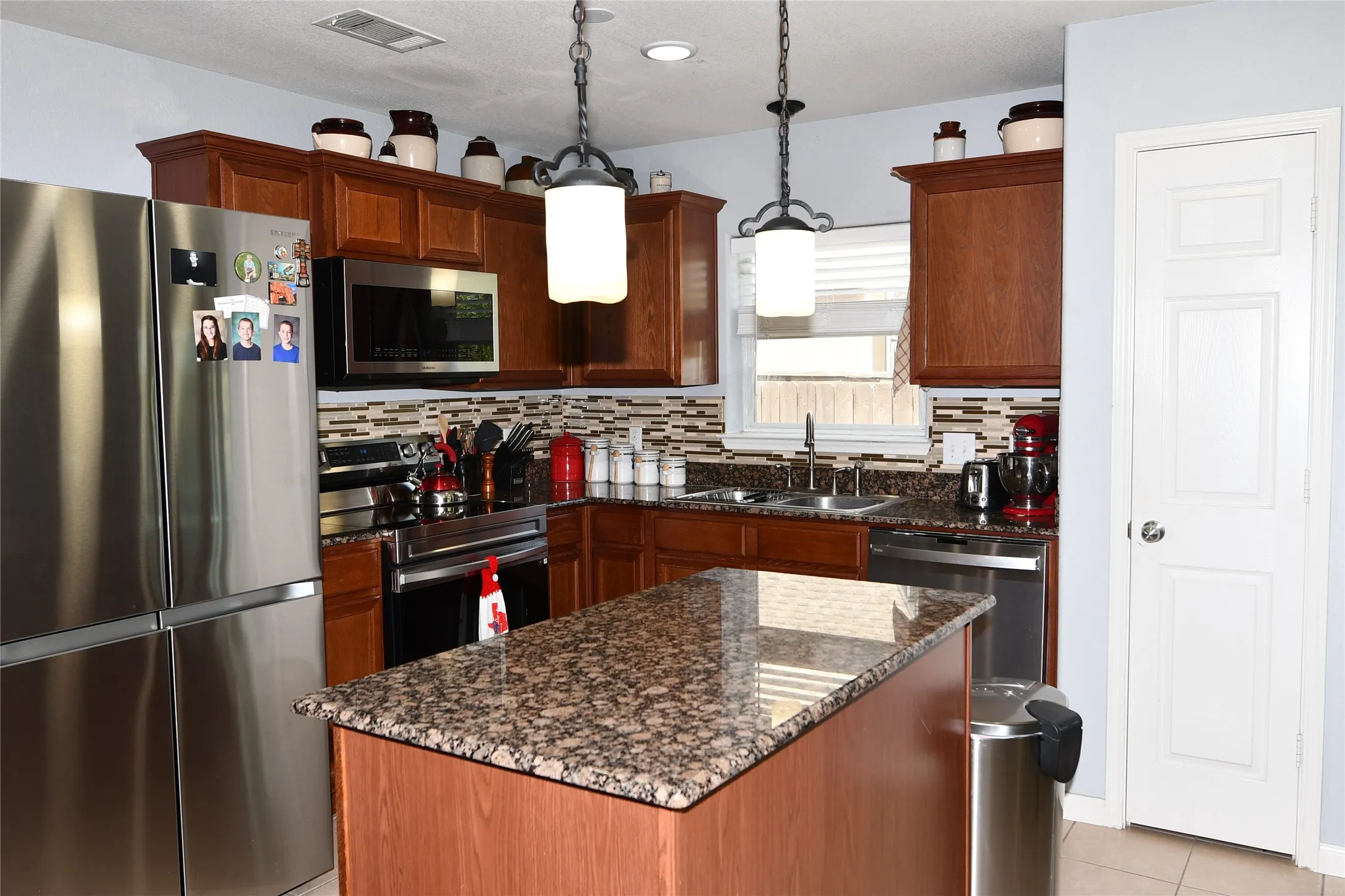 Kitchen featuring stainless steel appliances, wood-finish cabinetry, a central island with a stone-finish countertop, and a tiled backsplash