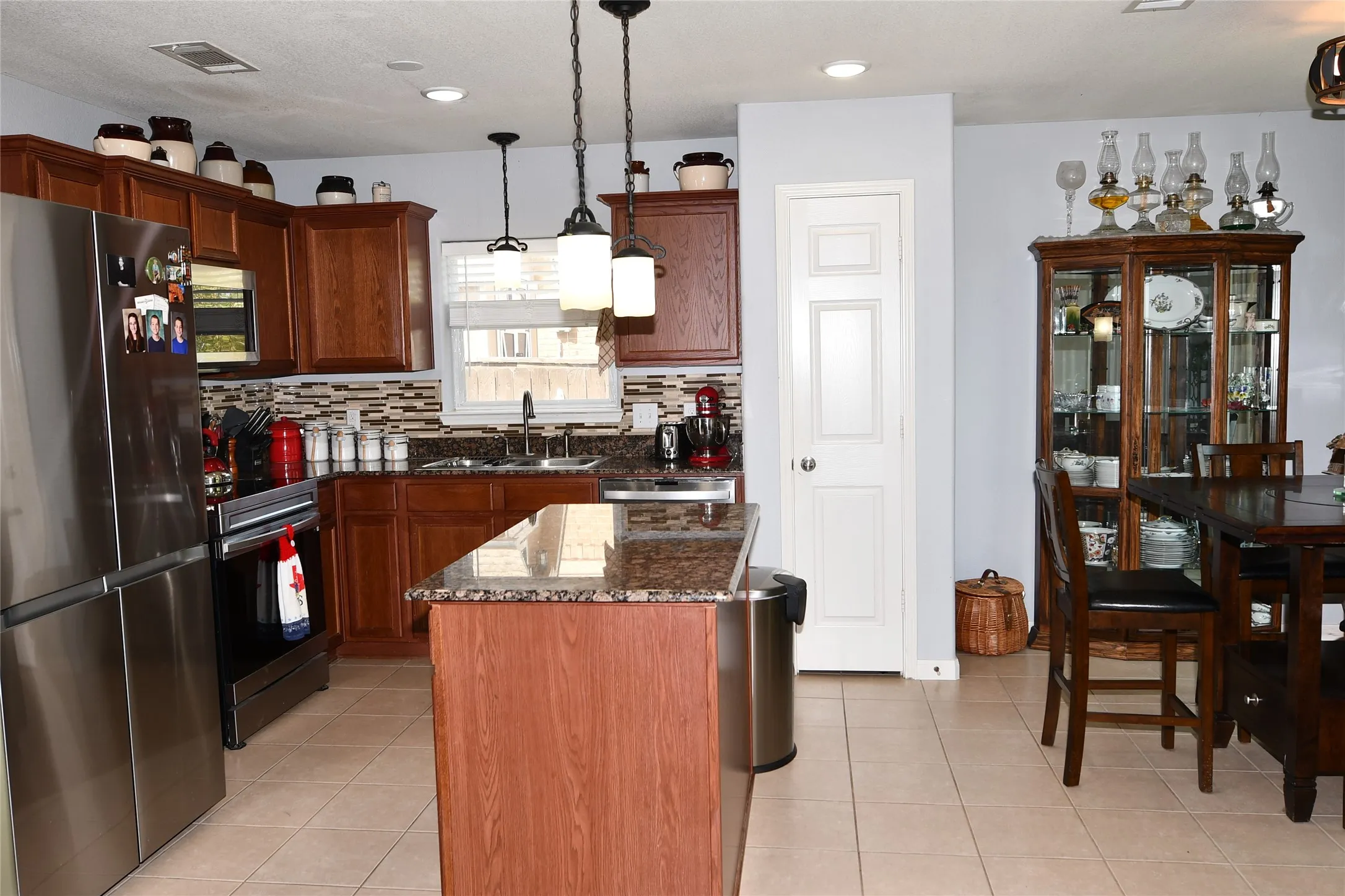 Kitchen featuring stainless steel appliances, wood cabinetry, granite countertops, and tile flooring