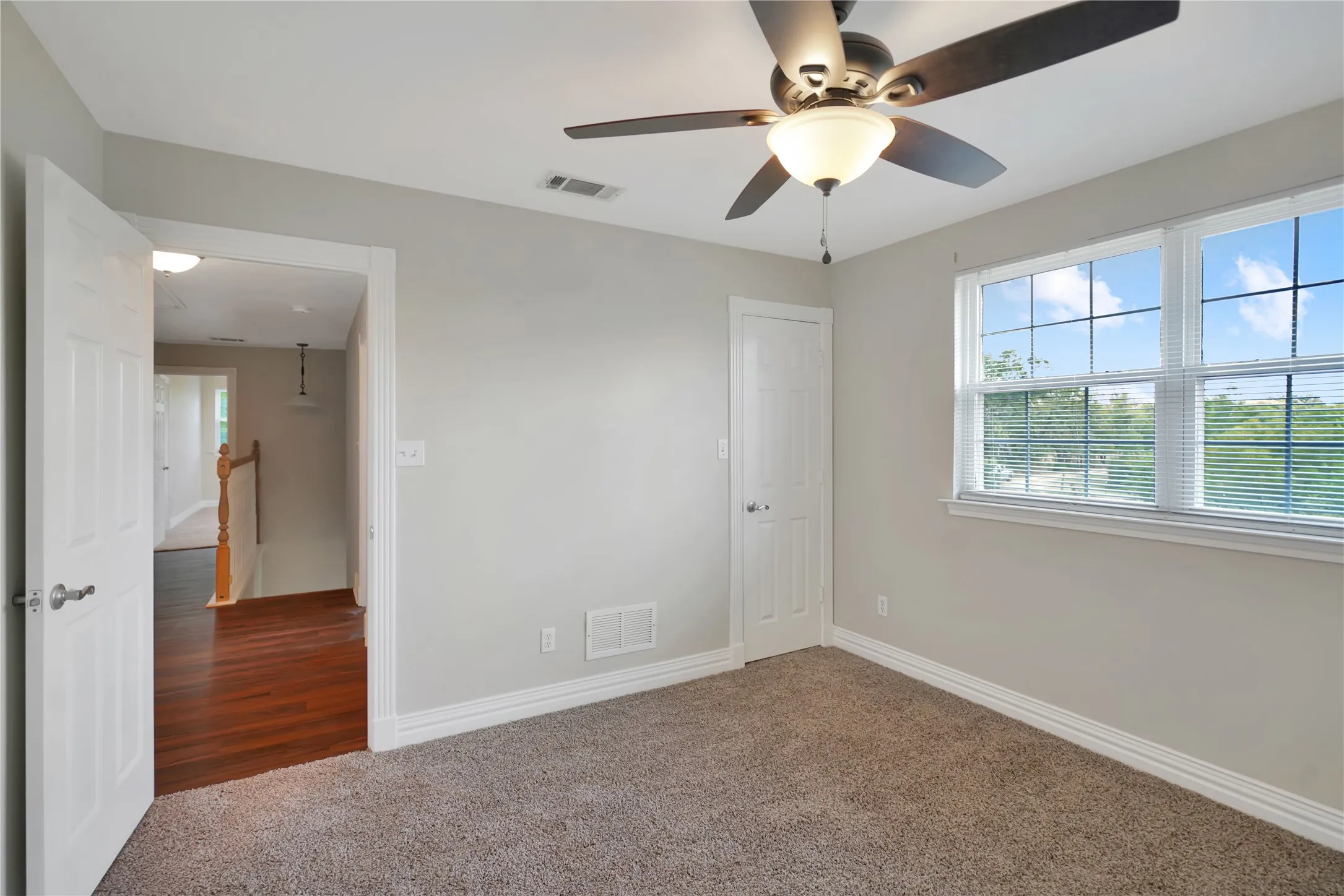 Carpeted room with a ceiling fan, dual windows, and white trim