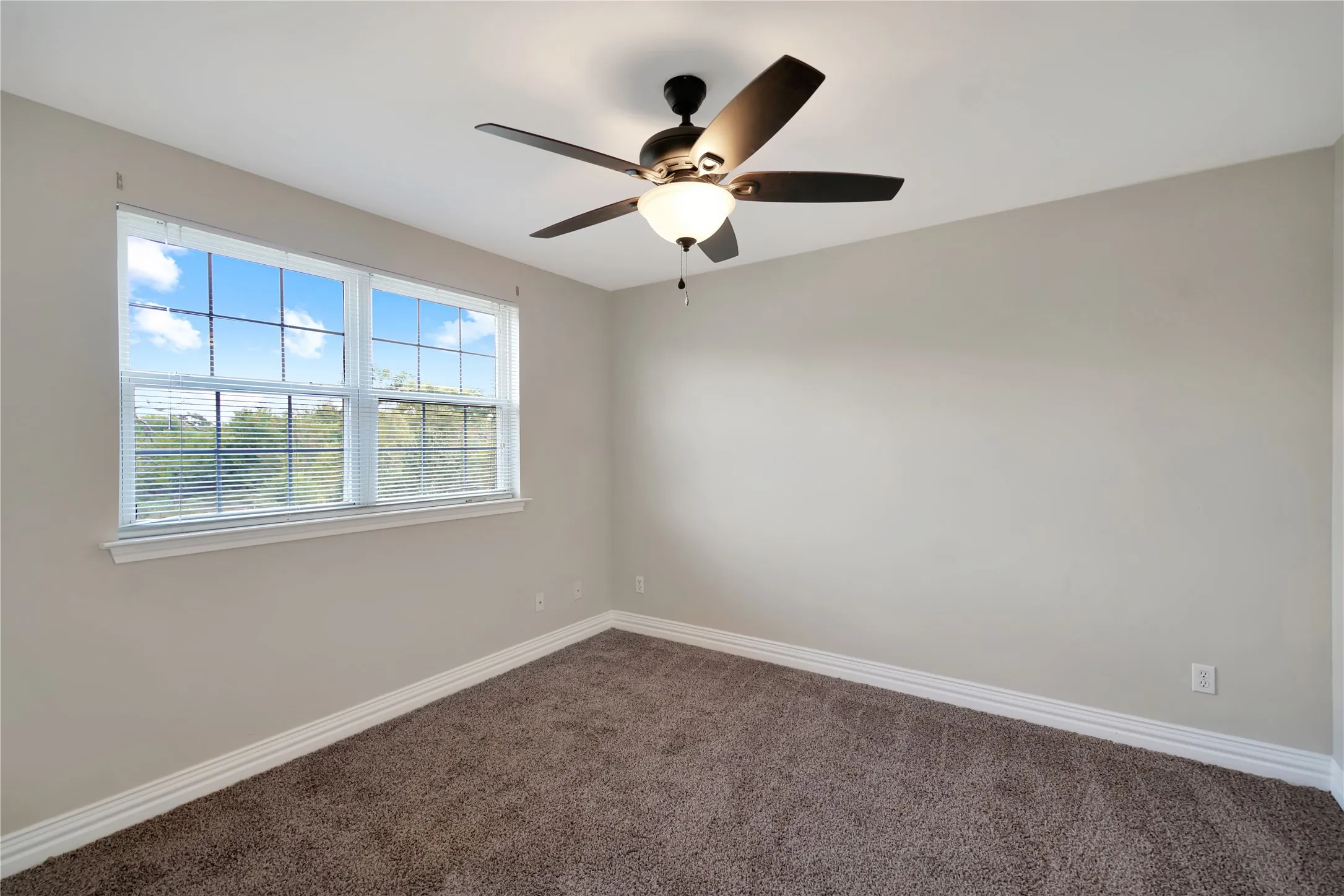 Neutral painted walls, plush carpet flooring, white window trim, and a ceiling fan with integrated lighting
