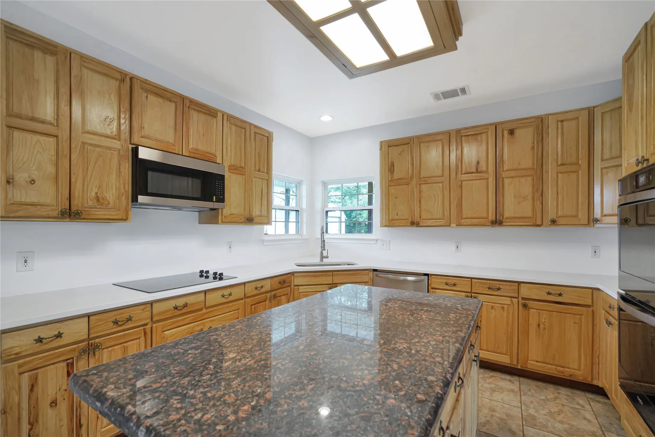 Kitchen with wood cabinetry, light-toned countertops, a center island with a dark countertop, and a built-in microwave