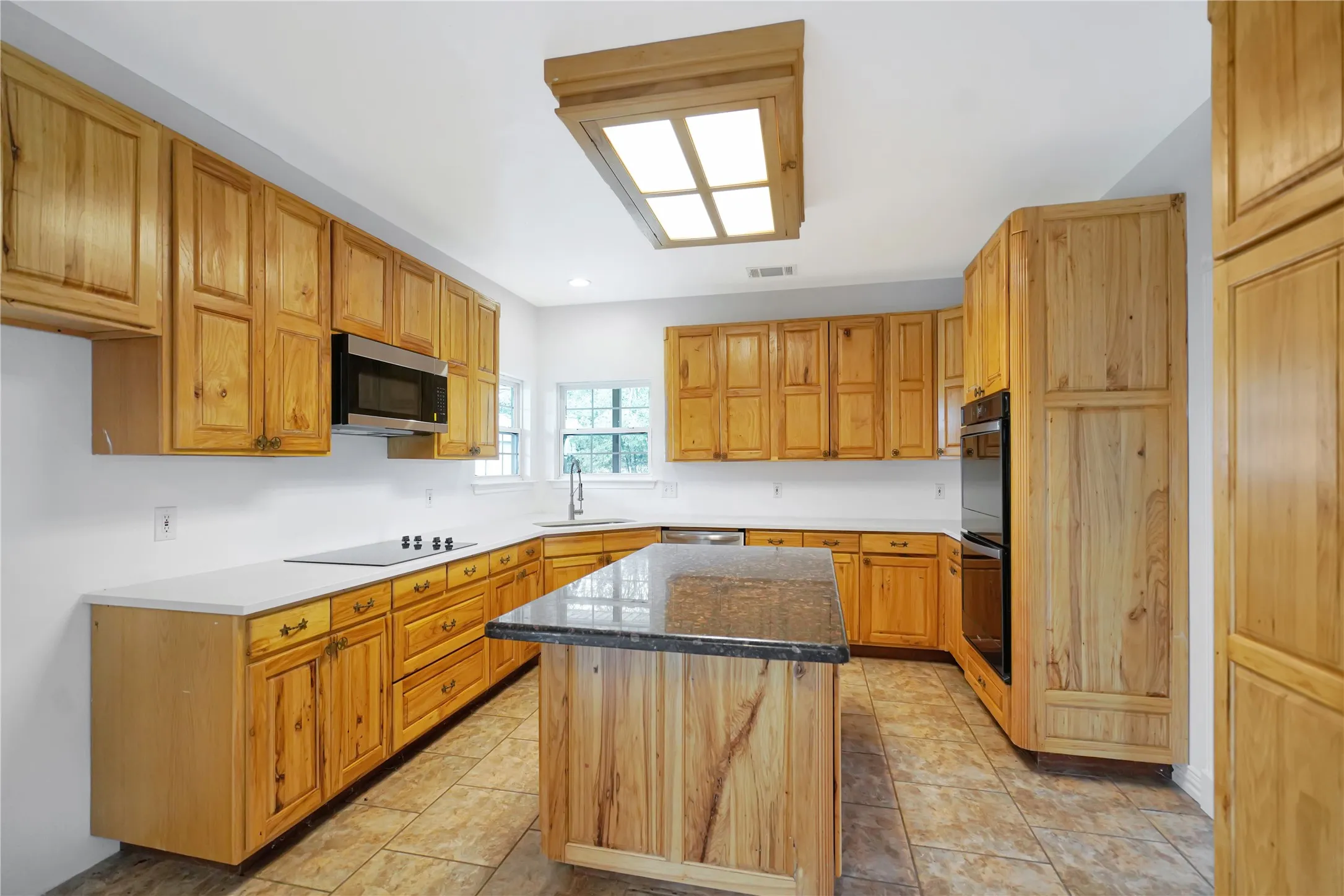 Kitchen featuring extensive wood cabinetry, white countertops, built-in double ovens, a center island with a dark stone countertop, and tile flooring