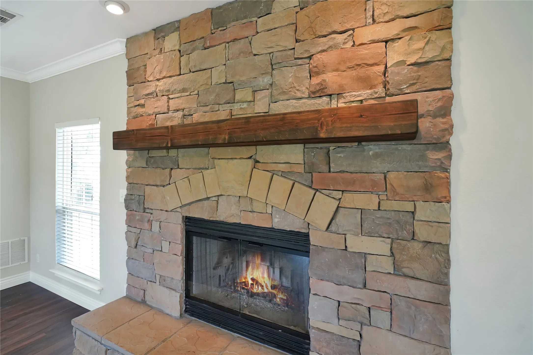 Stone-clad fireplace featuring an arched firebox with a glass door, a substantial wood mantel, and a hearth