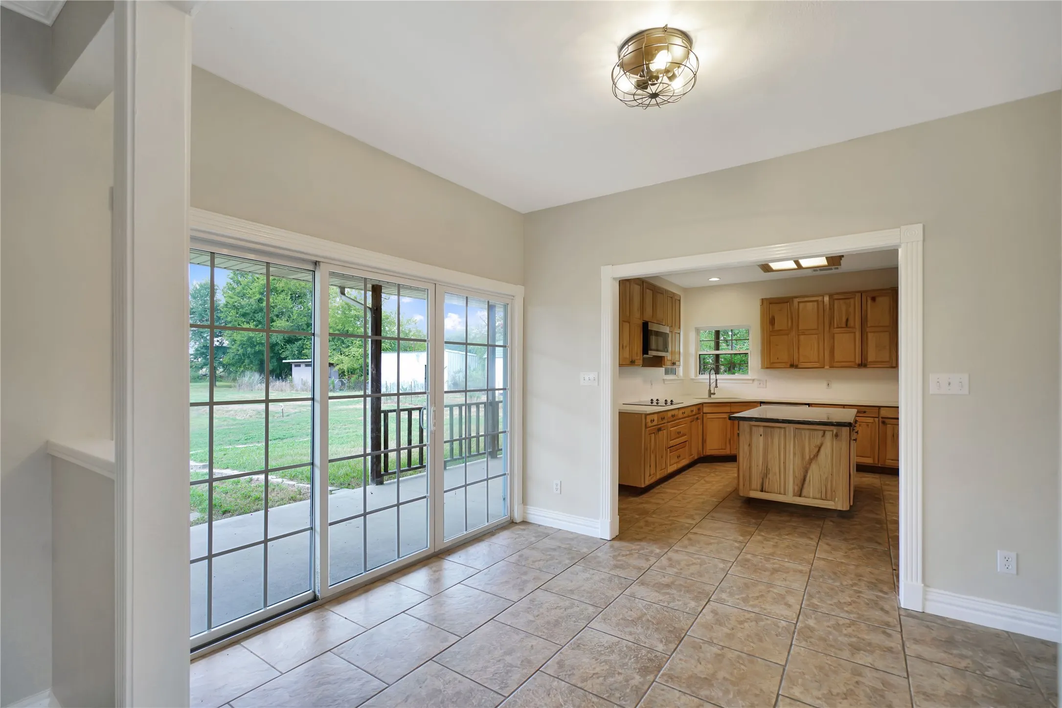 Spacious interior with tile flooring throughout, a modern ceiling light fixture, and large sliding glass doors opening to an exterior patio