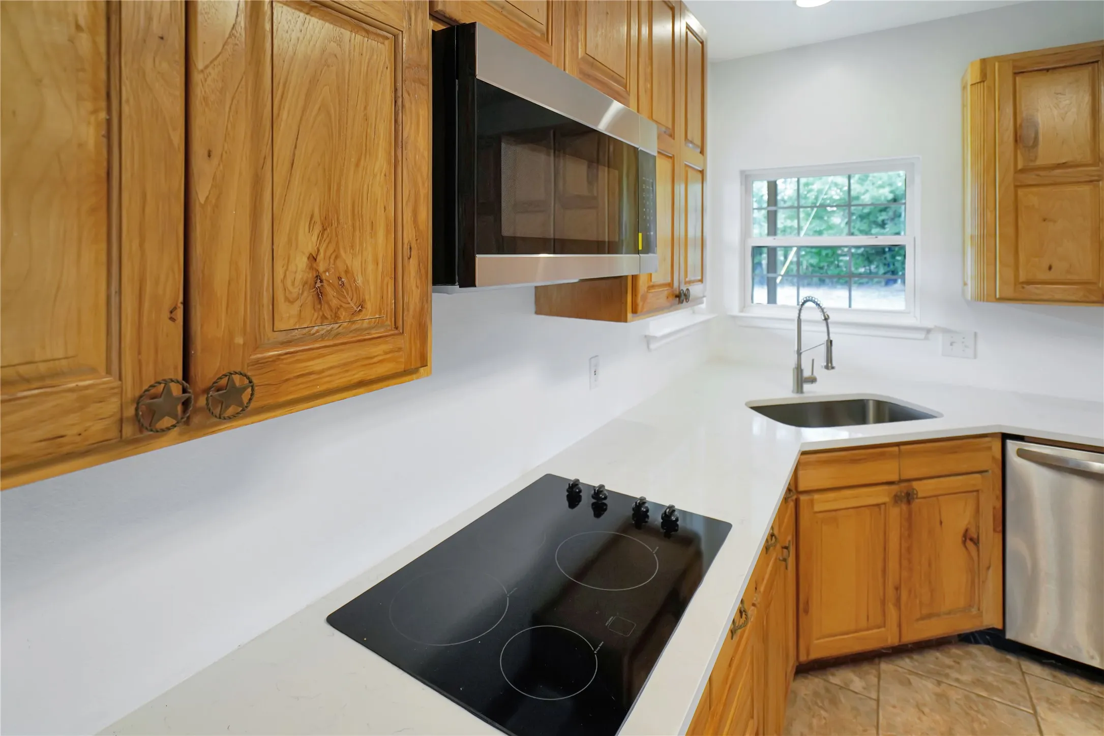 Kitchen featuring wood cabinetry, white countertops, built-in stainless steel microwave, stainless steel sink with gooseneck faucet, and a black cooktop