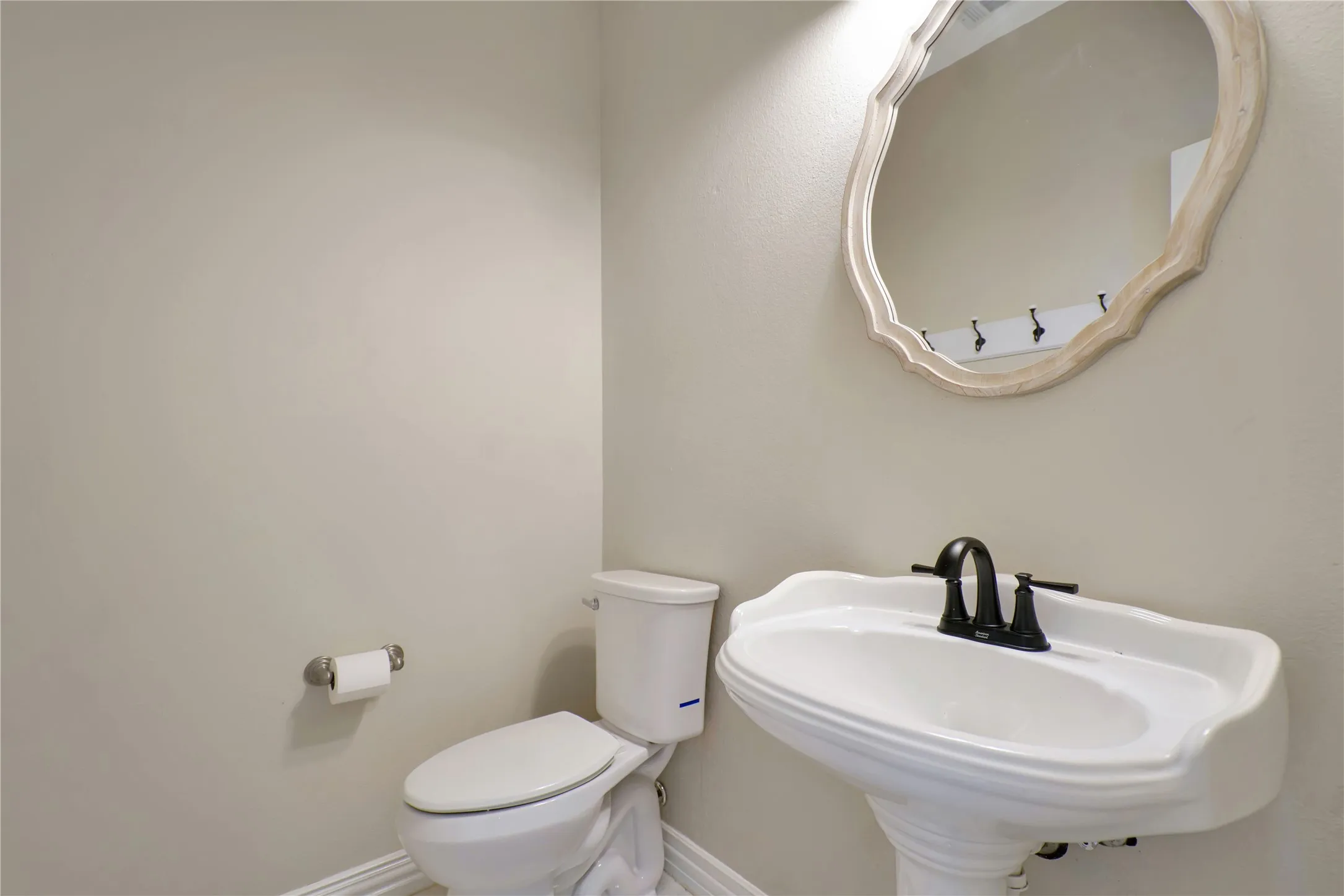 White pedestal sink with a dark bronze faucet, white toilet, and a decorative mirror with a light-toned frame