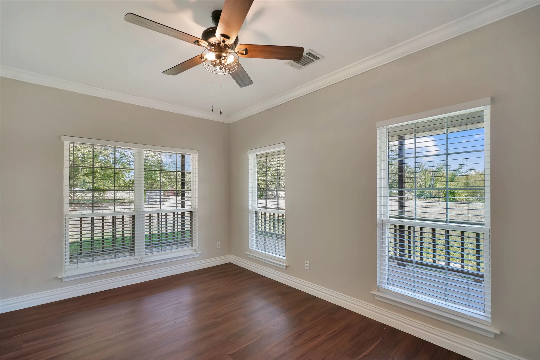 Wood-finish flooring, crown molding, white trim, and a ceiling fan with integrated lighting