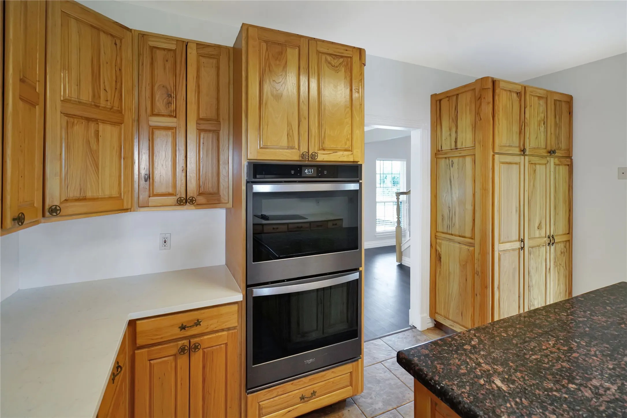 Wood-finish cabinetry, stainless steel double wall oven, light-toned countertop, and brown speckled countertop
