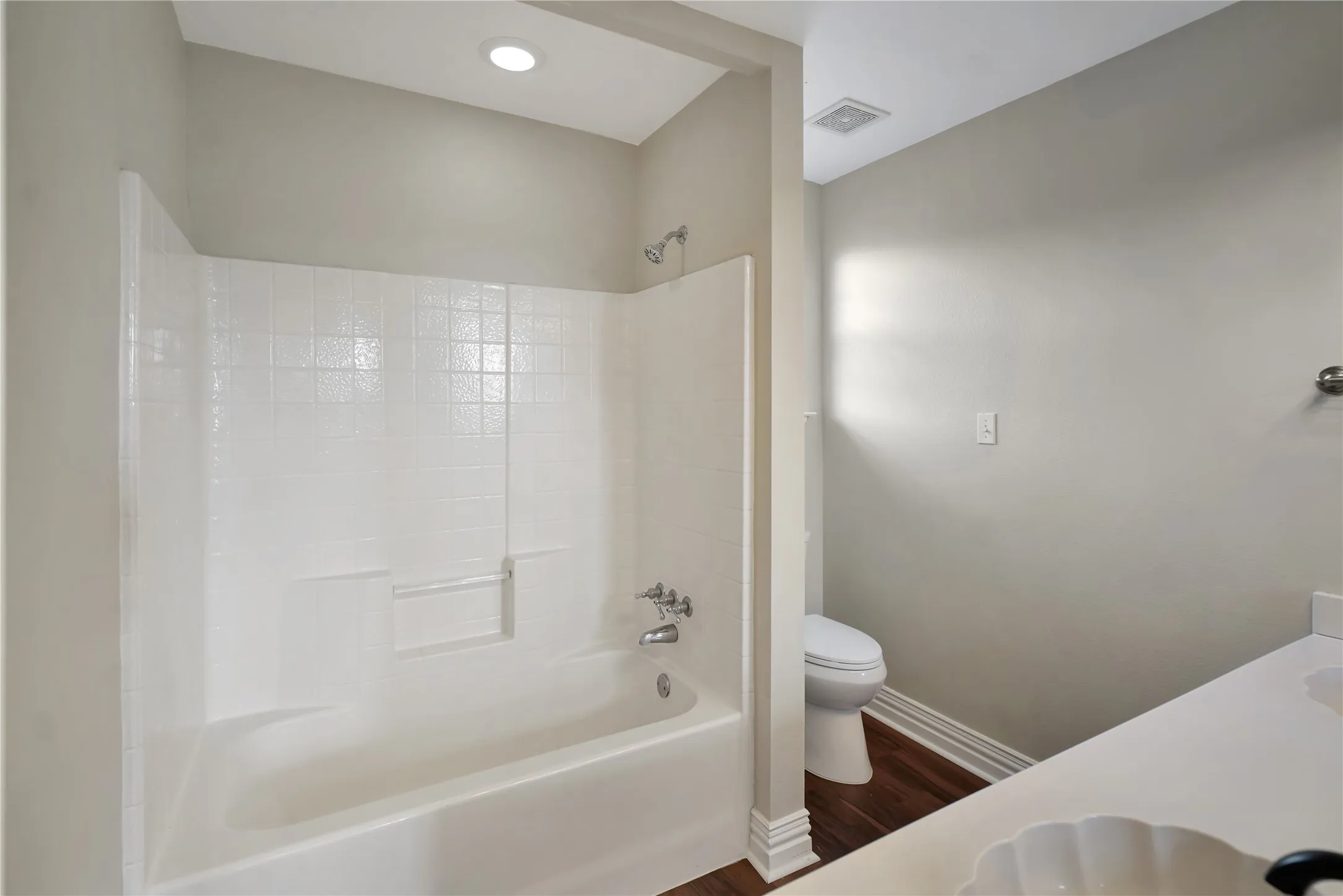 Bathtub with integrated shower, white tiled surround, and chrome fixtures