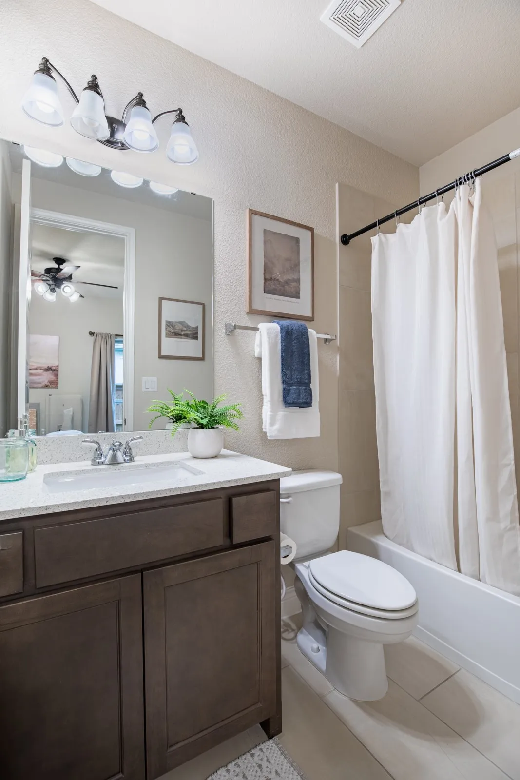 Vanity with a light-toned countertop and an integrated sink, dark wood-finish cabinetry, a rectangular wall mirror, and a white bathtub with a shower rod
