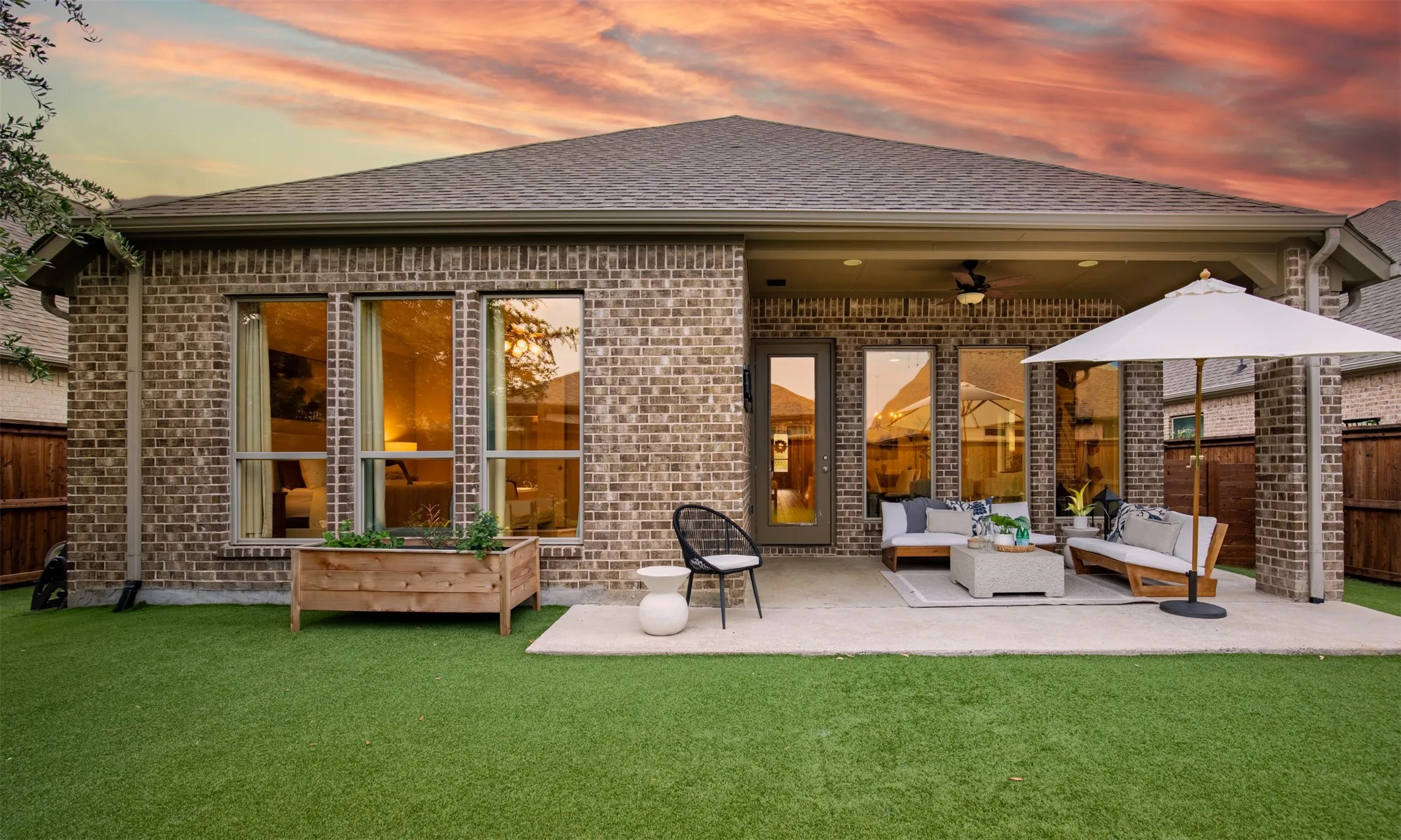 Brick exterior with multiple windows, covered patio, concrete patio, and artificial turf