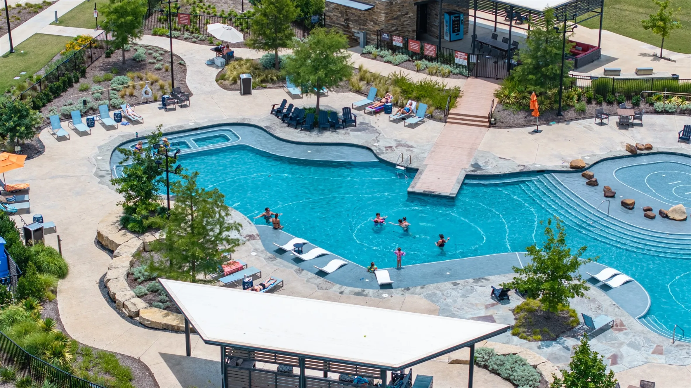 Expansive swimming pool with integrated hot tub, multiple lounging areas, mature landscaping, and a covered patio structure