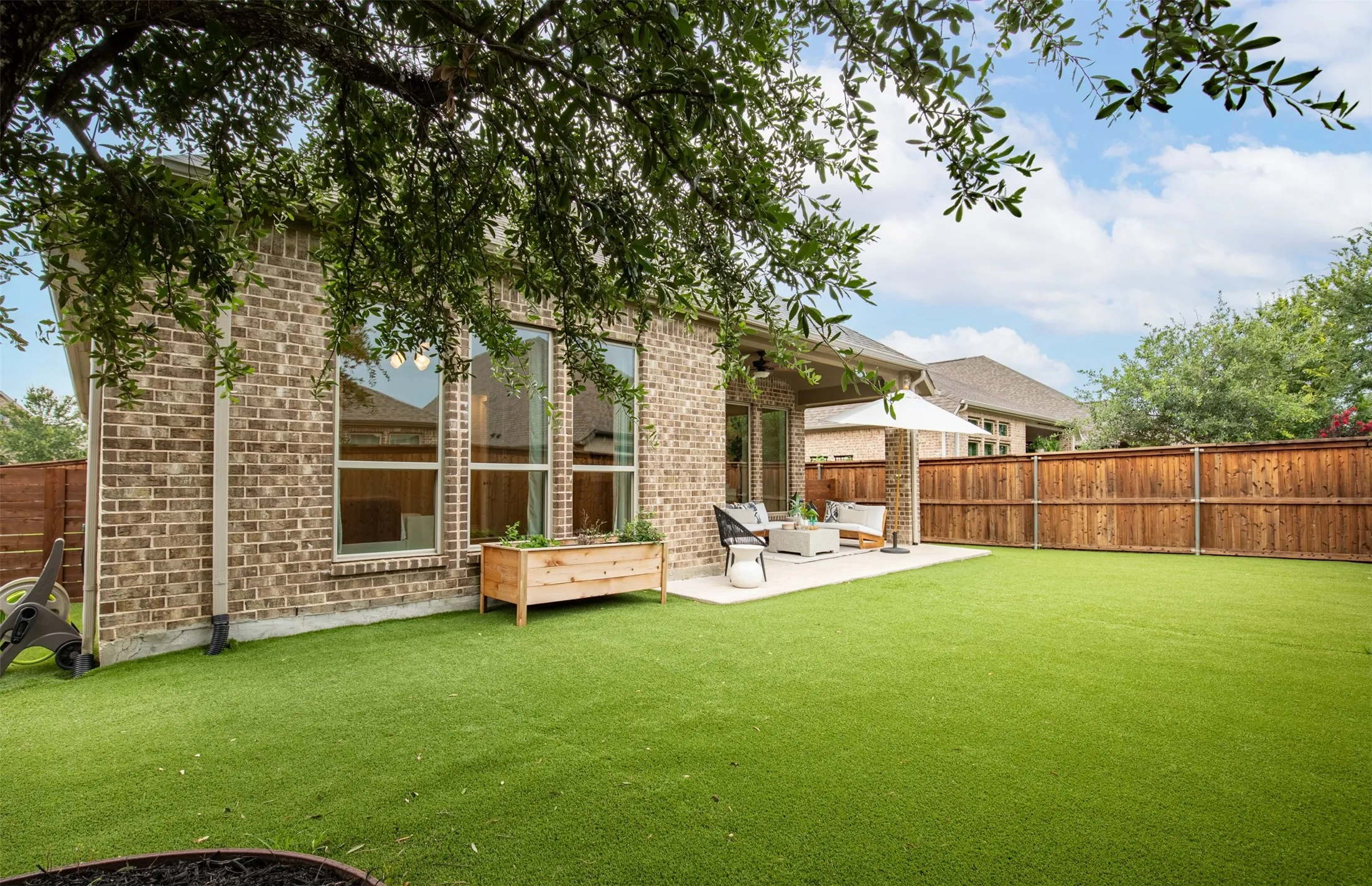 Expansive artificial turf lawn, privacy fencing, brick exterior, large windows, and a concrete patio