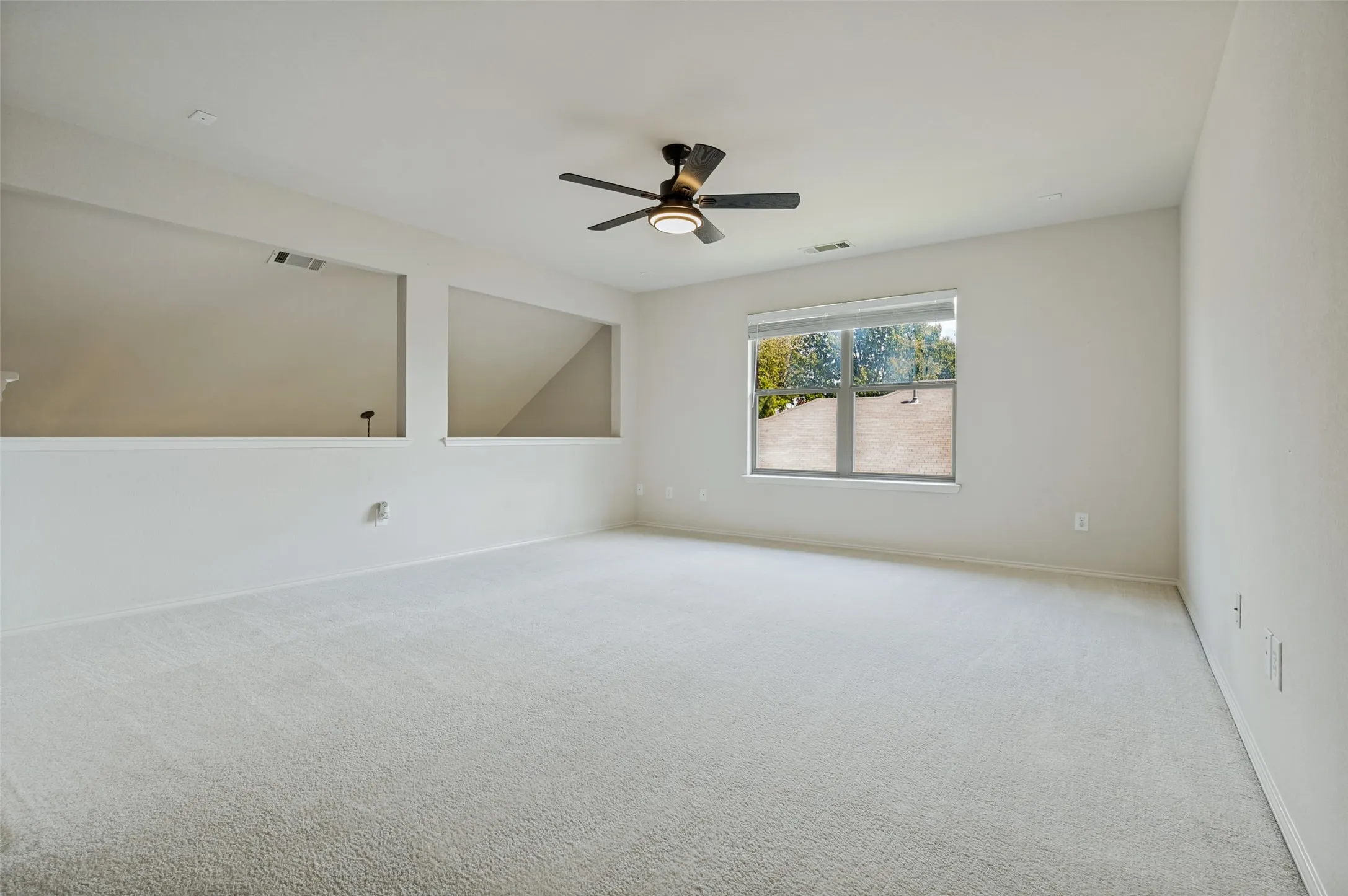 Expansive carpeted area with a ceiling fan and natural light from a large window