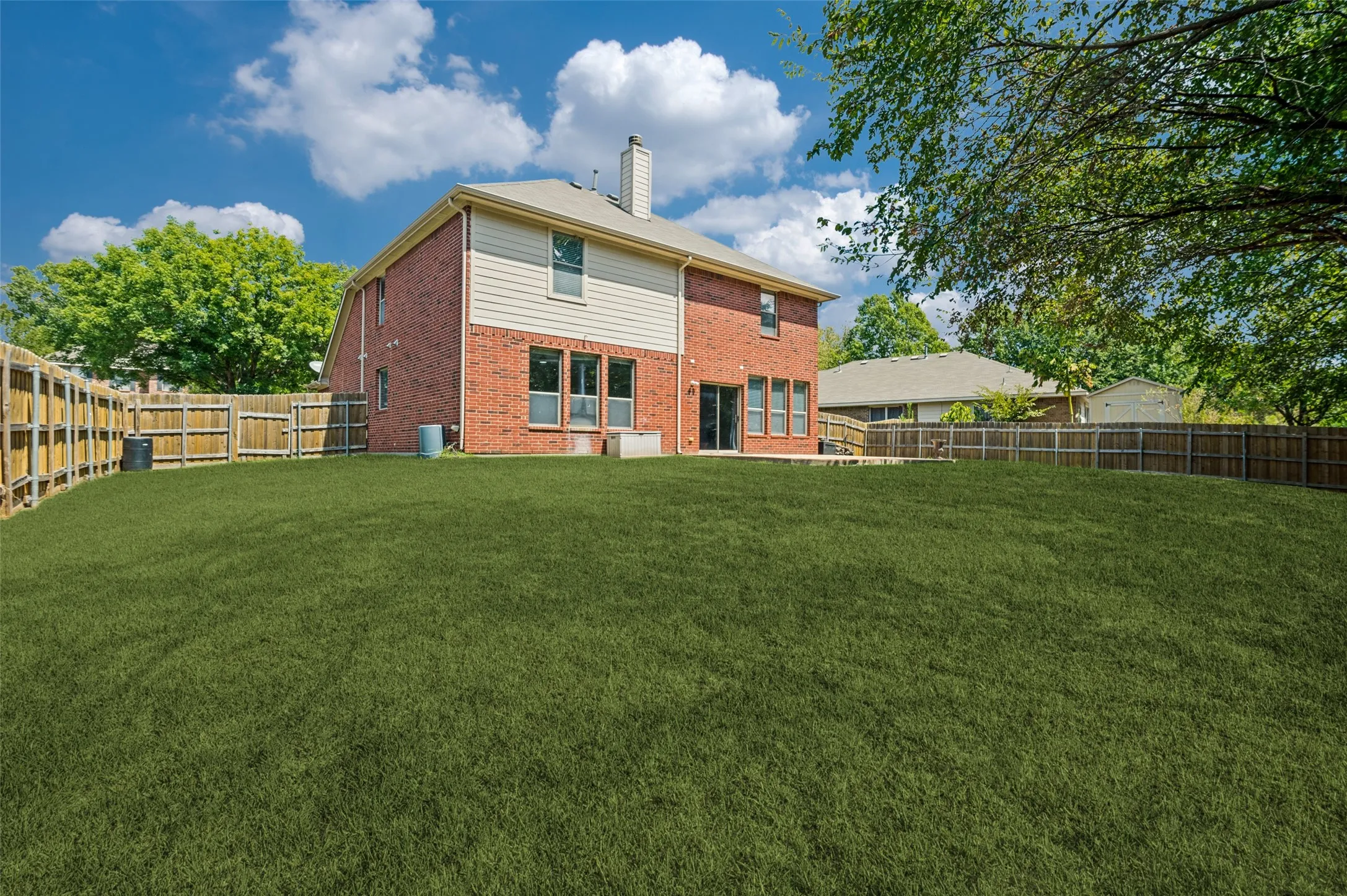 Expansive fenced yard featuring a manicured lawn, red brick exterior, and a two-story residential structure with a shingled roof