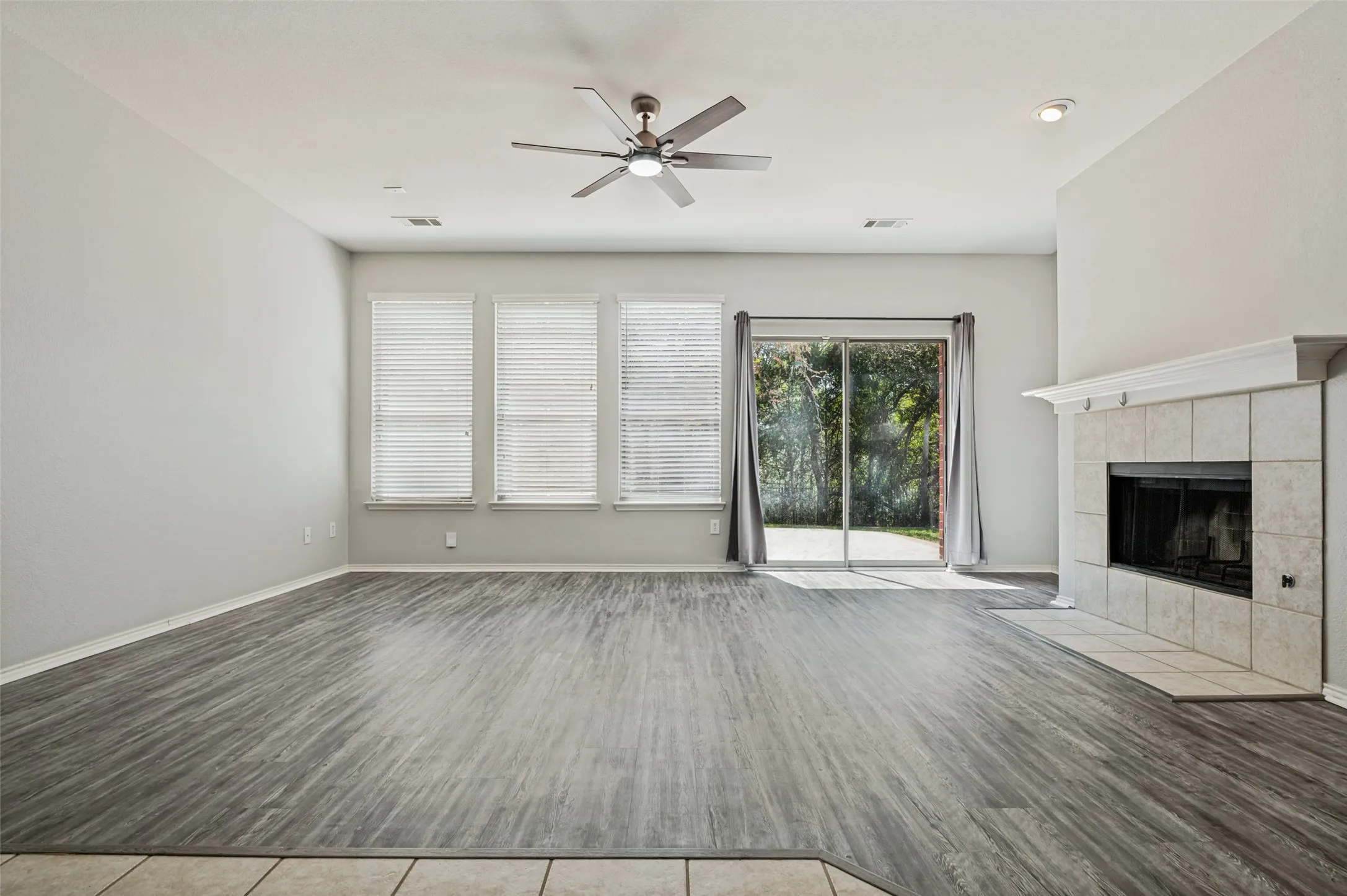 Tile-surrounded fireplace with a white mantel, wood-finish flooring, multiple windows, and a sliding glass door