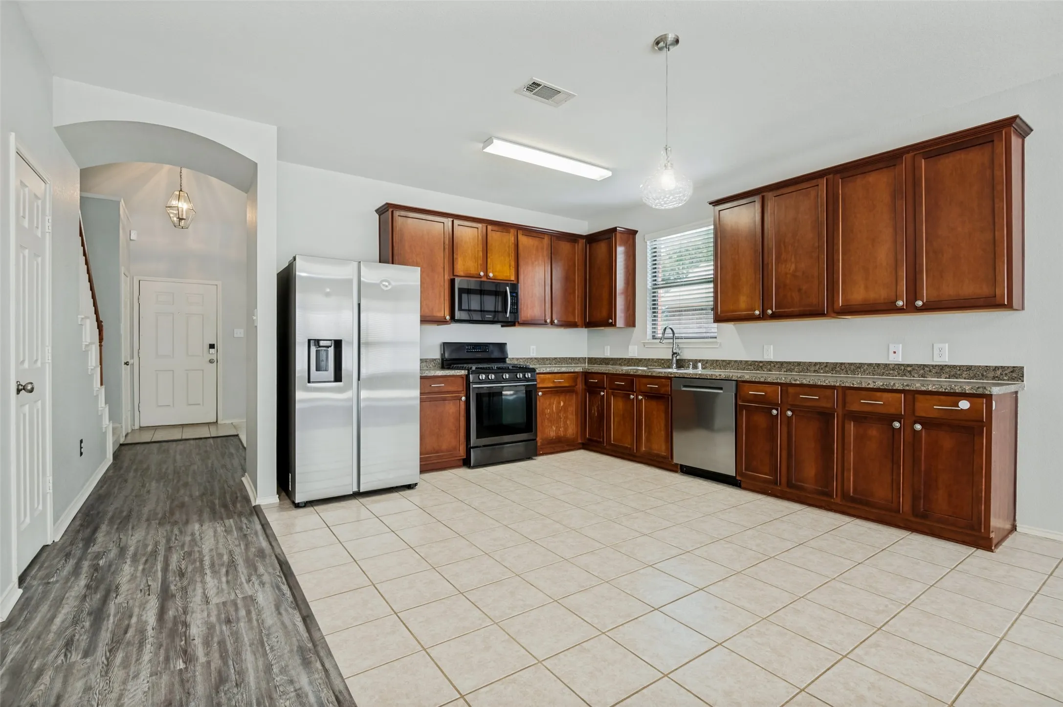 Kitchen featuring extensive wood cabinetry, stone-finish countertops, stainless steel appliances, and tile flooring