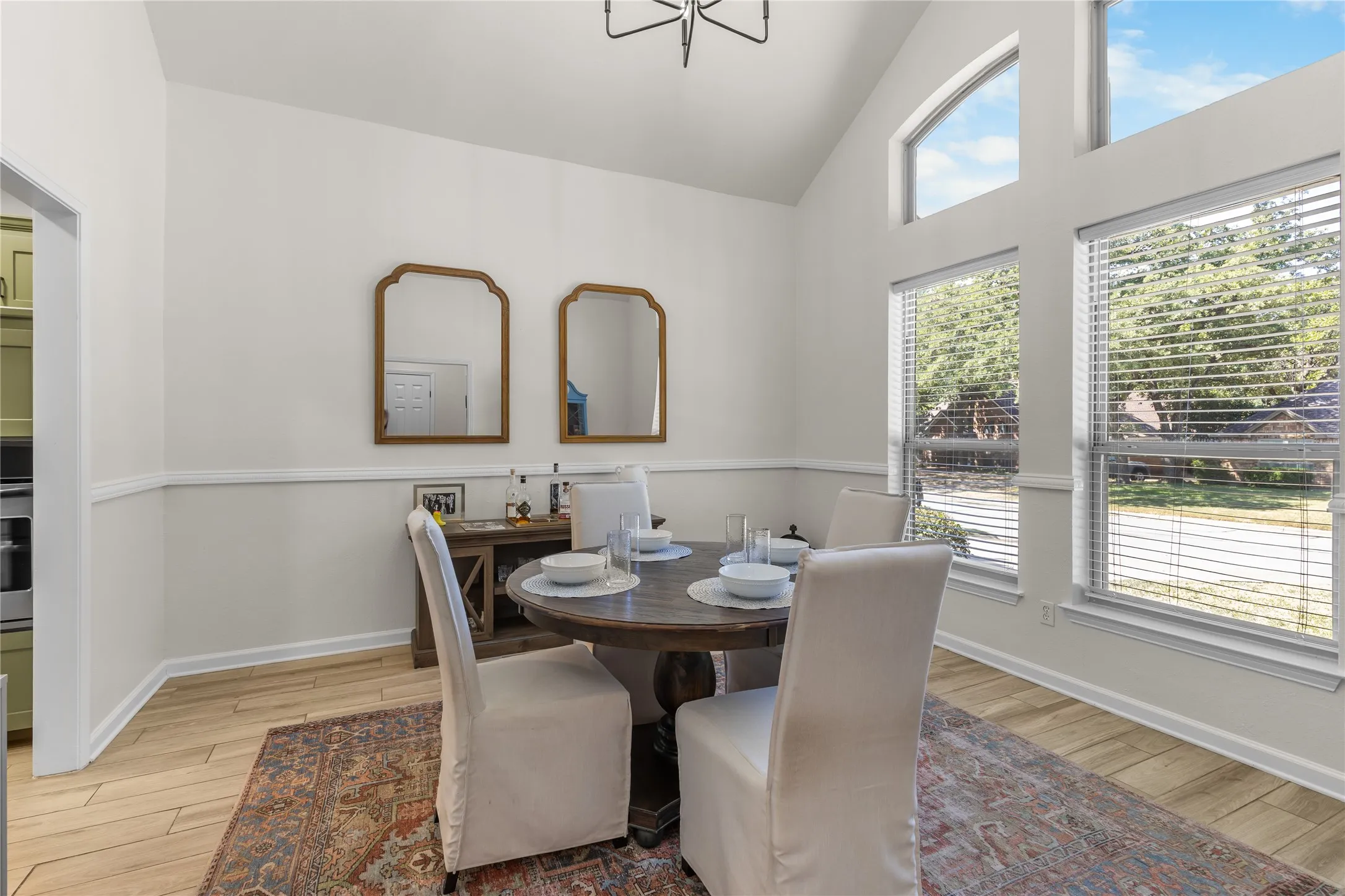Vaulted ceiling with a contemporary light fixture, large windows with blinds, wood-finish flooring, and white painted walls
