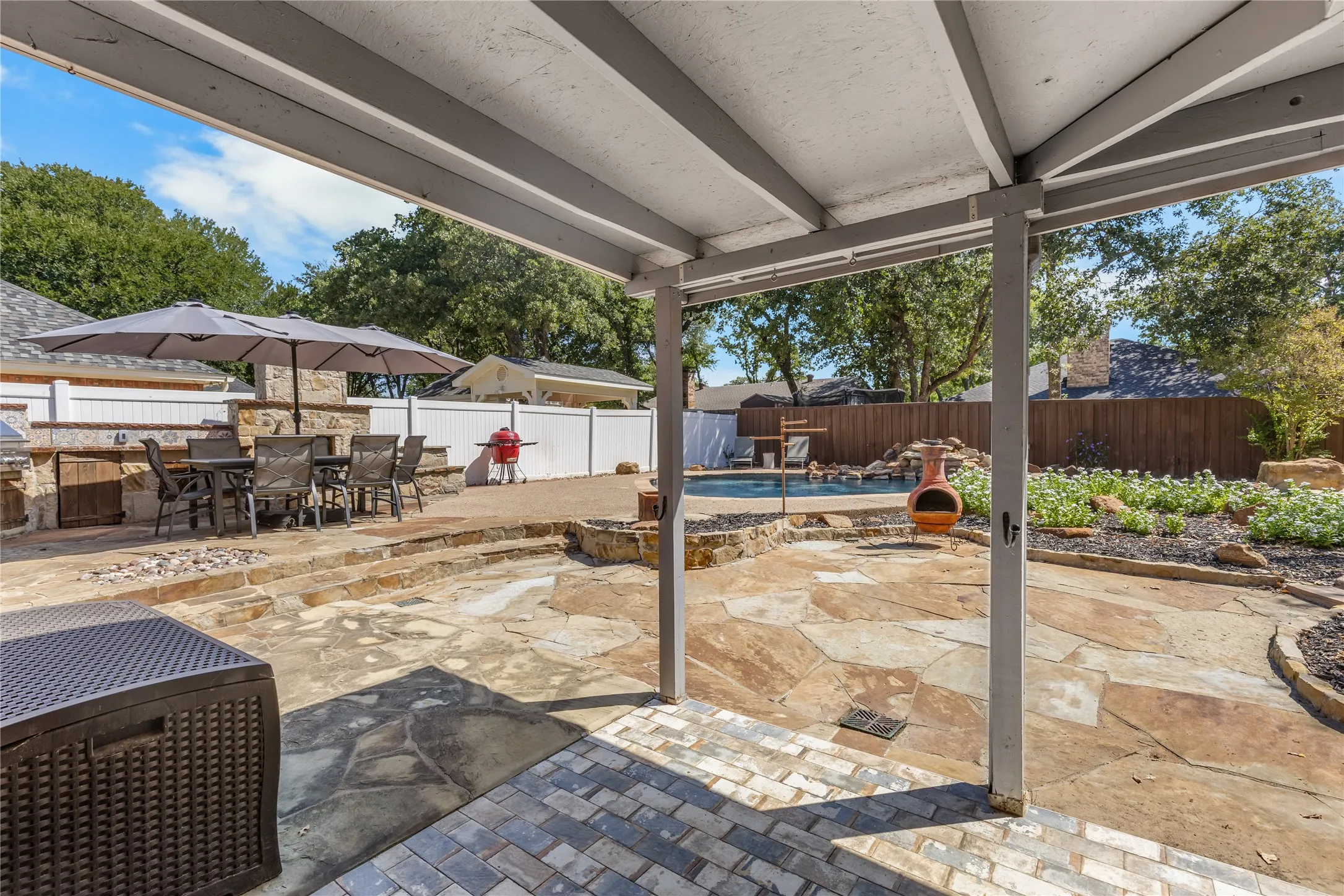 Covered patio with a brick paver surface, stone-paved outdoor living area, built-in outdoor kitchen, and a swimming pool with a rock waterfall feature