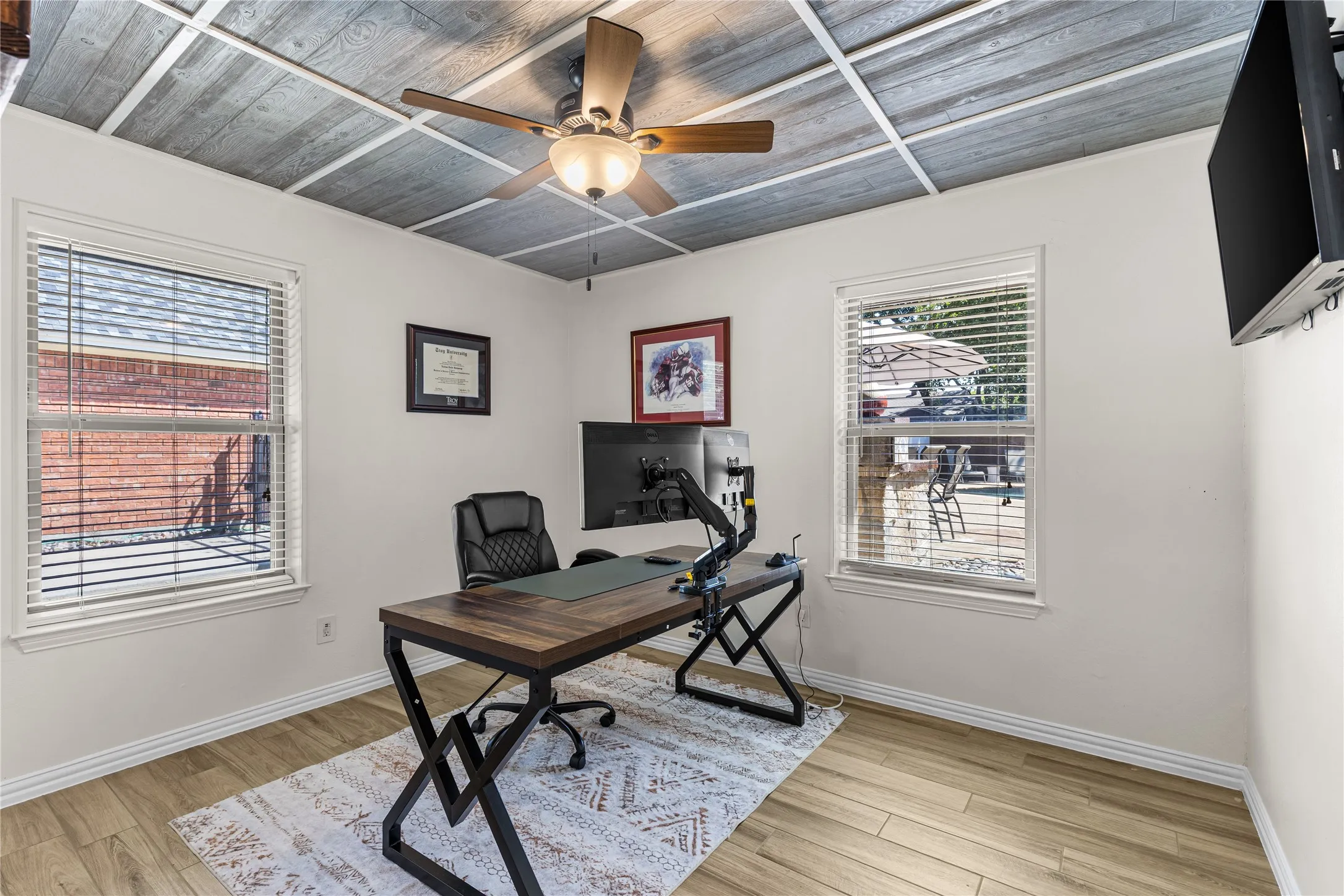Wood-finish flooring, white walls, and a gray wood-plank ceiling with white trim, featuring a ceiling fan