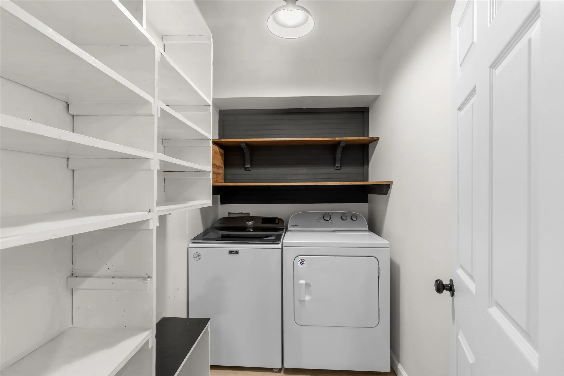 Built-in shelving, two wood-finish floating shelves, light wood-finish flooring, white panel door, overhead lighting fixture