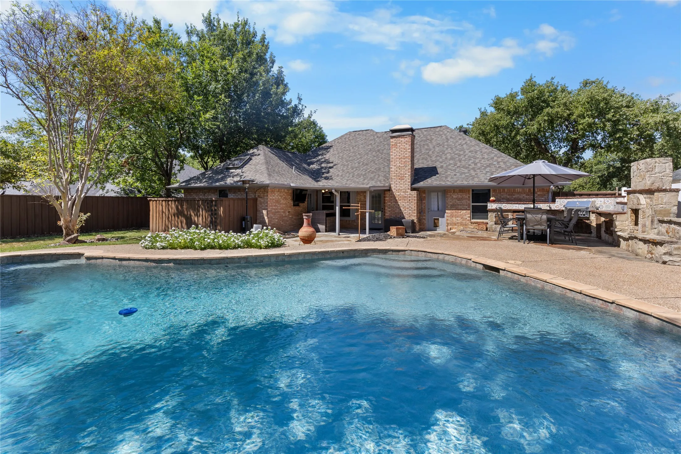 Expansive backyard featuring a large swimming pool, brick exterior, and a stone outdoor kitchen with a built-in grill