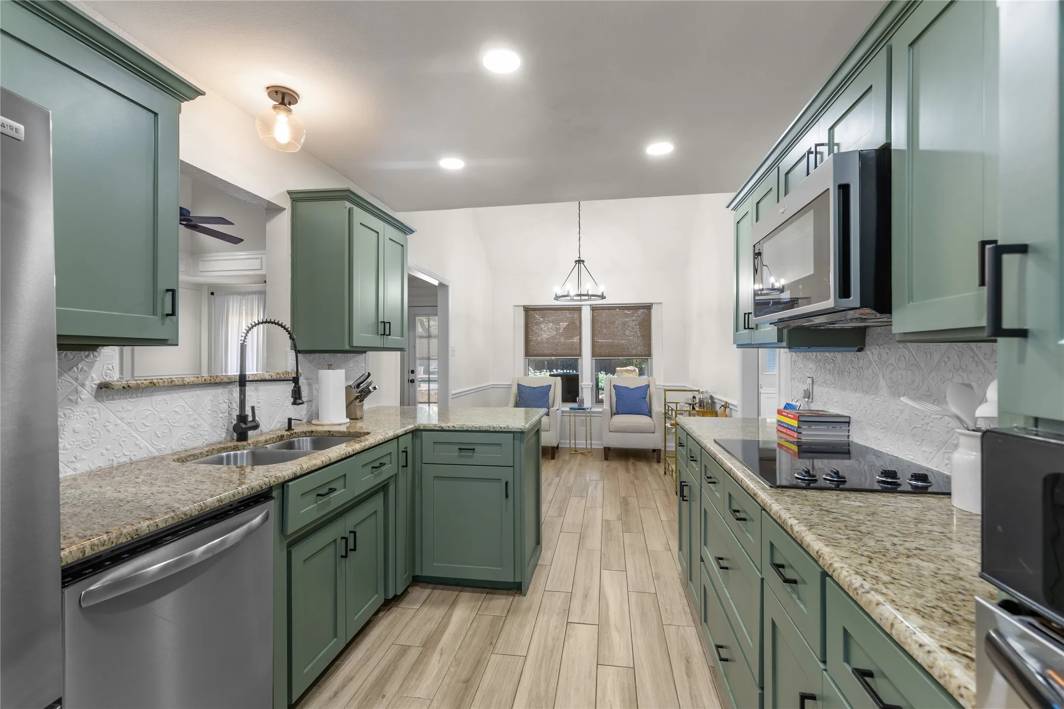 Open-concept kitchen featuring sage cabinetry, granite countertops, tile backsplash, stainless steel appliances, and wood-finish flooring