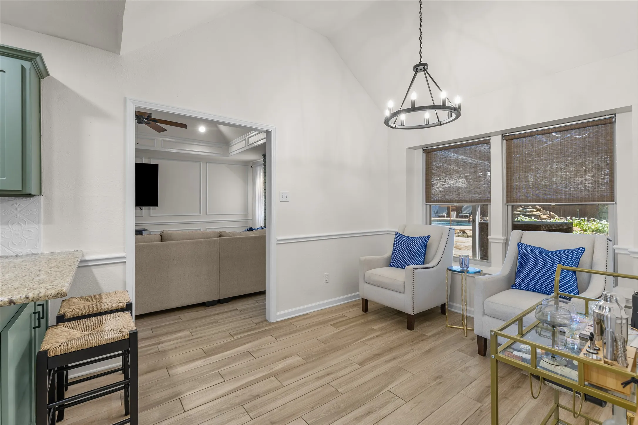 Vaulted ceiling with an iron chandelier, wood-finish flooring, two large windows with blinds, and wainscoting