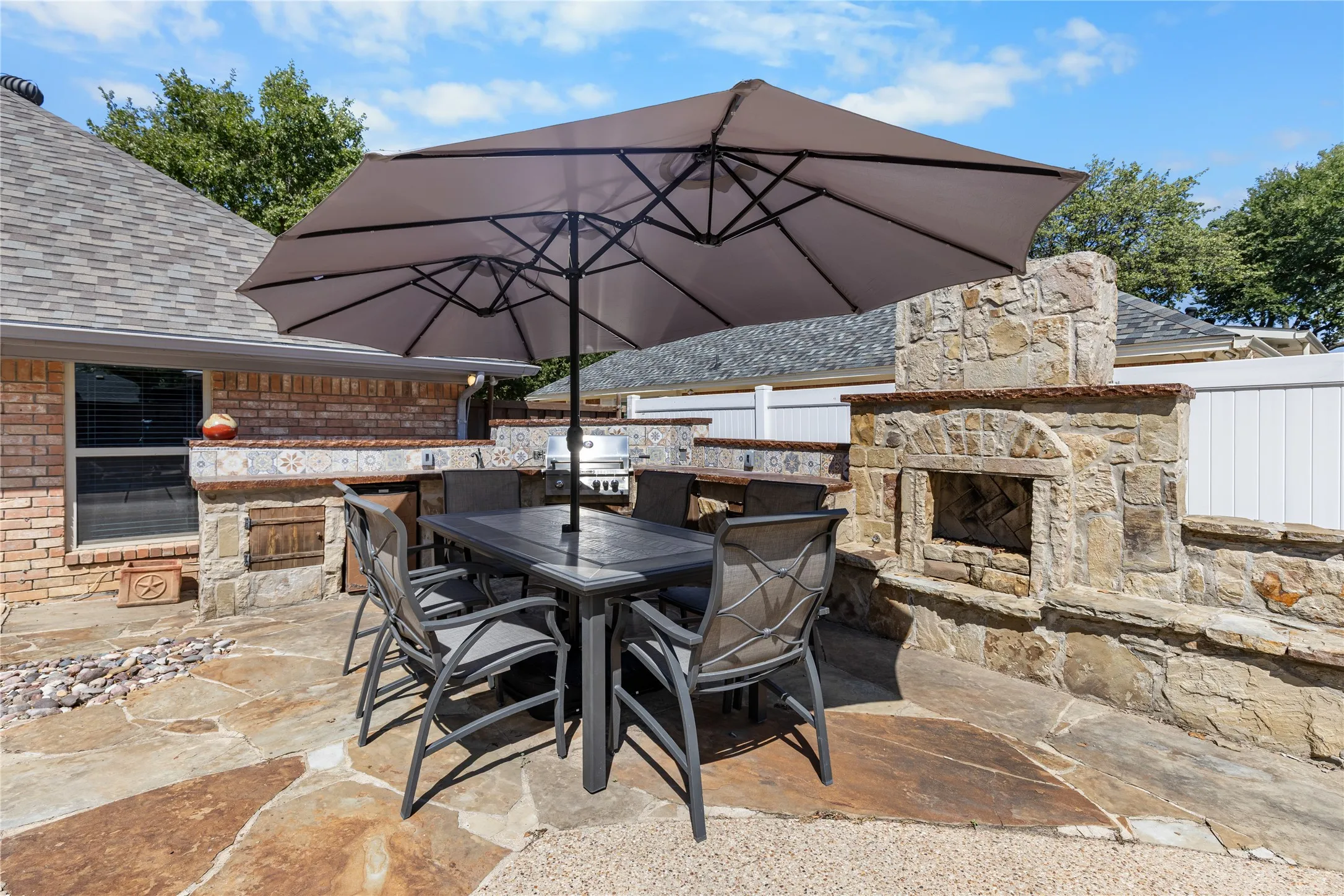 Flagstone patio with a stone outdoor fireplace, built-in stone and tile counter, and a privacy fence