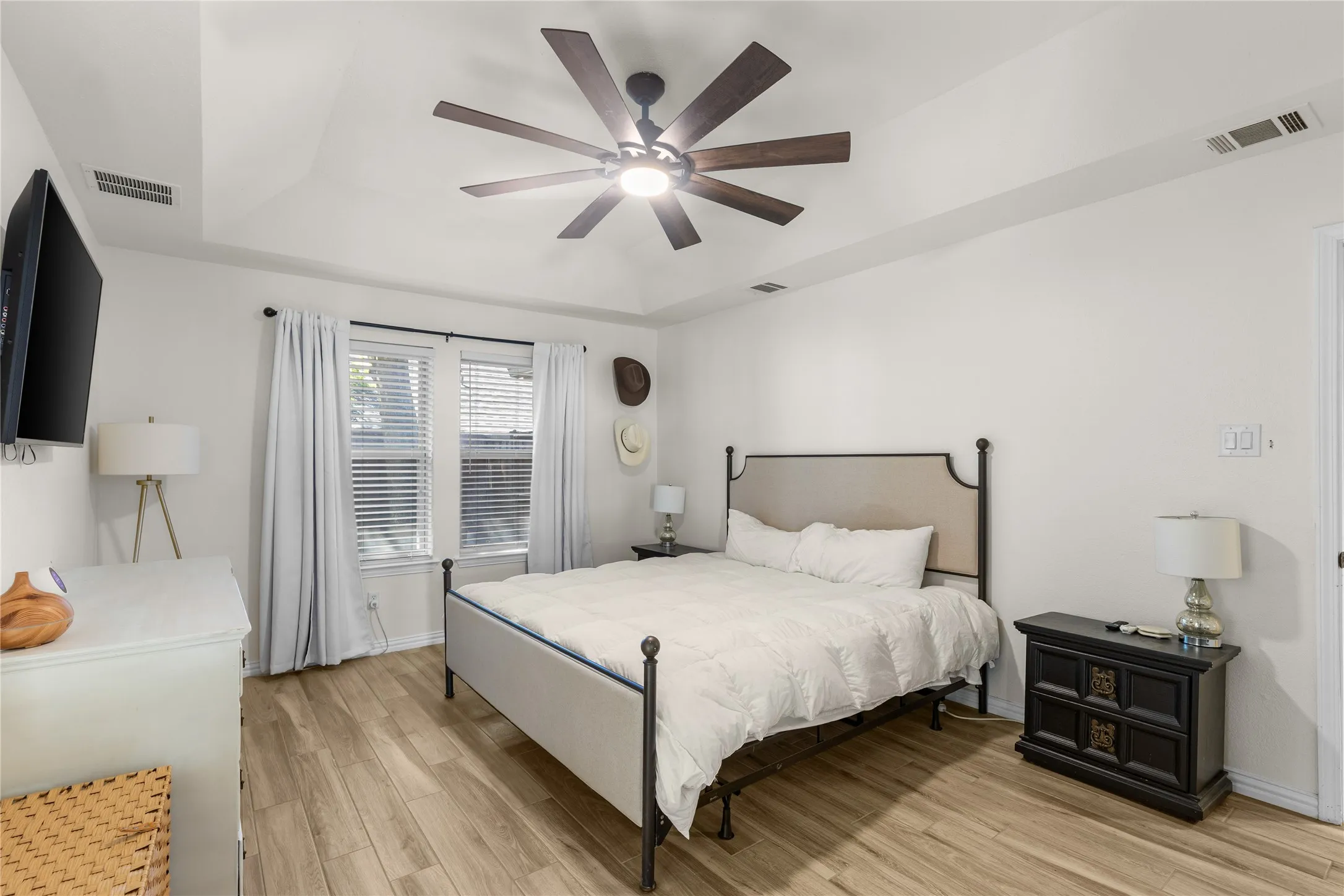 Tray ceiling with a ceiling fan, wood-finish flooring, and white window blinds