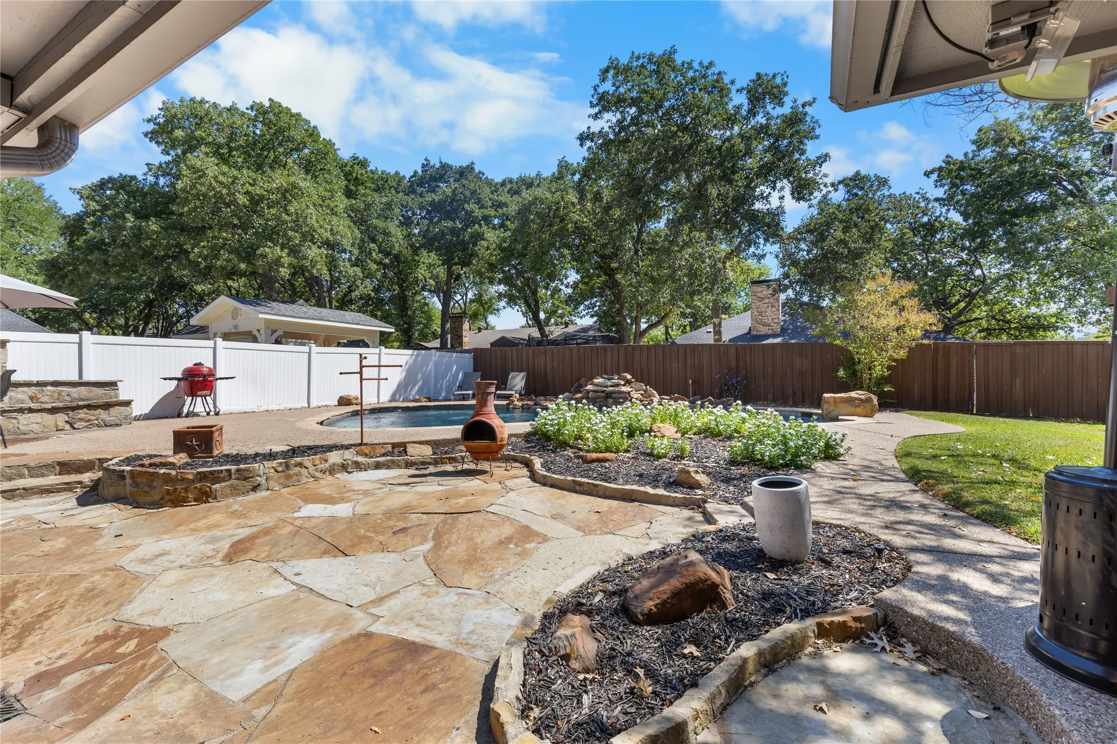 Expansive outdoor living area featuring a custom stone patio, a built-in fire pit, a swimming pool with a rock waterfall, and a manicured lawn